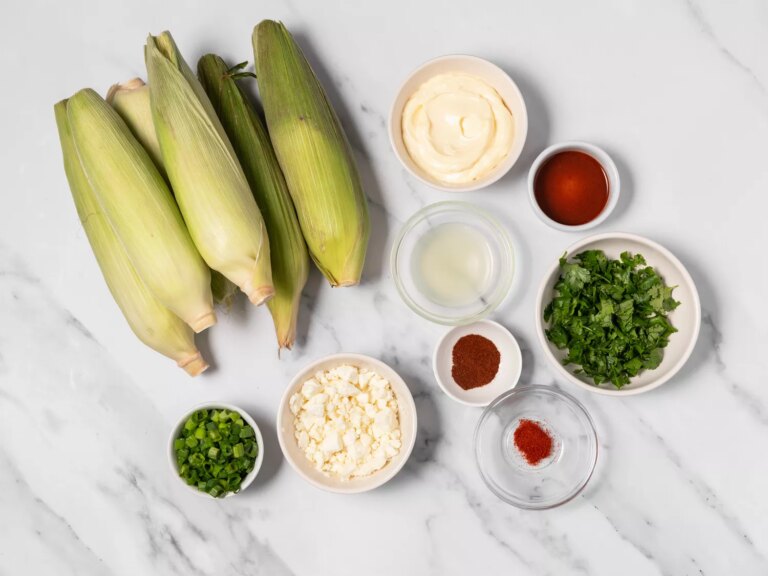 Fresh uncooked ears of corn with various ingredients for elote salad.