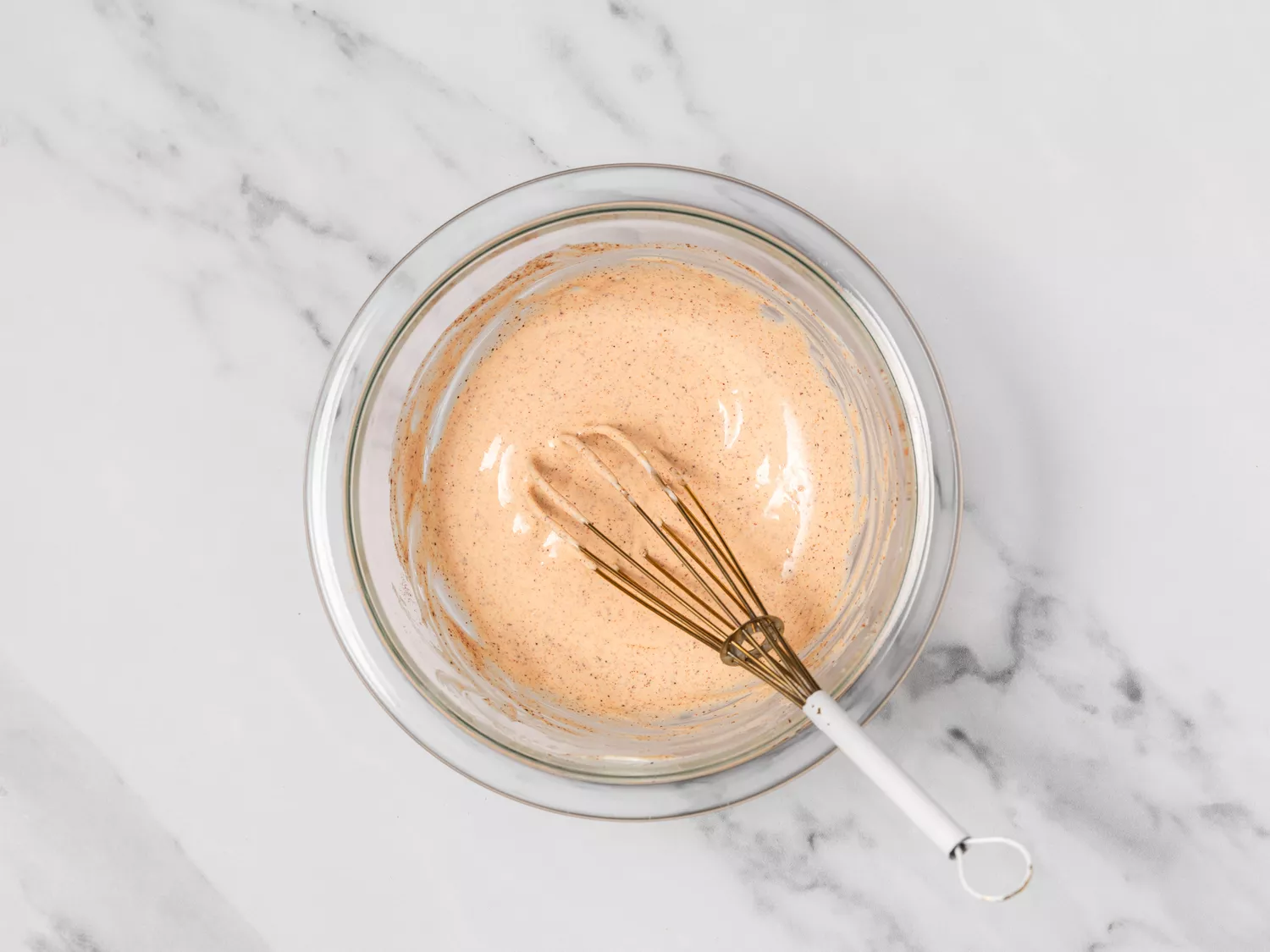 Spicy mayo dressing in a glass bowl with a whisk.