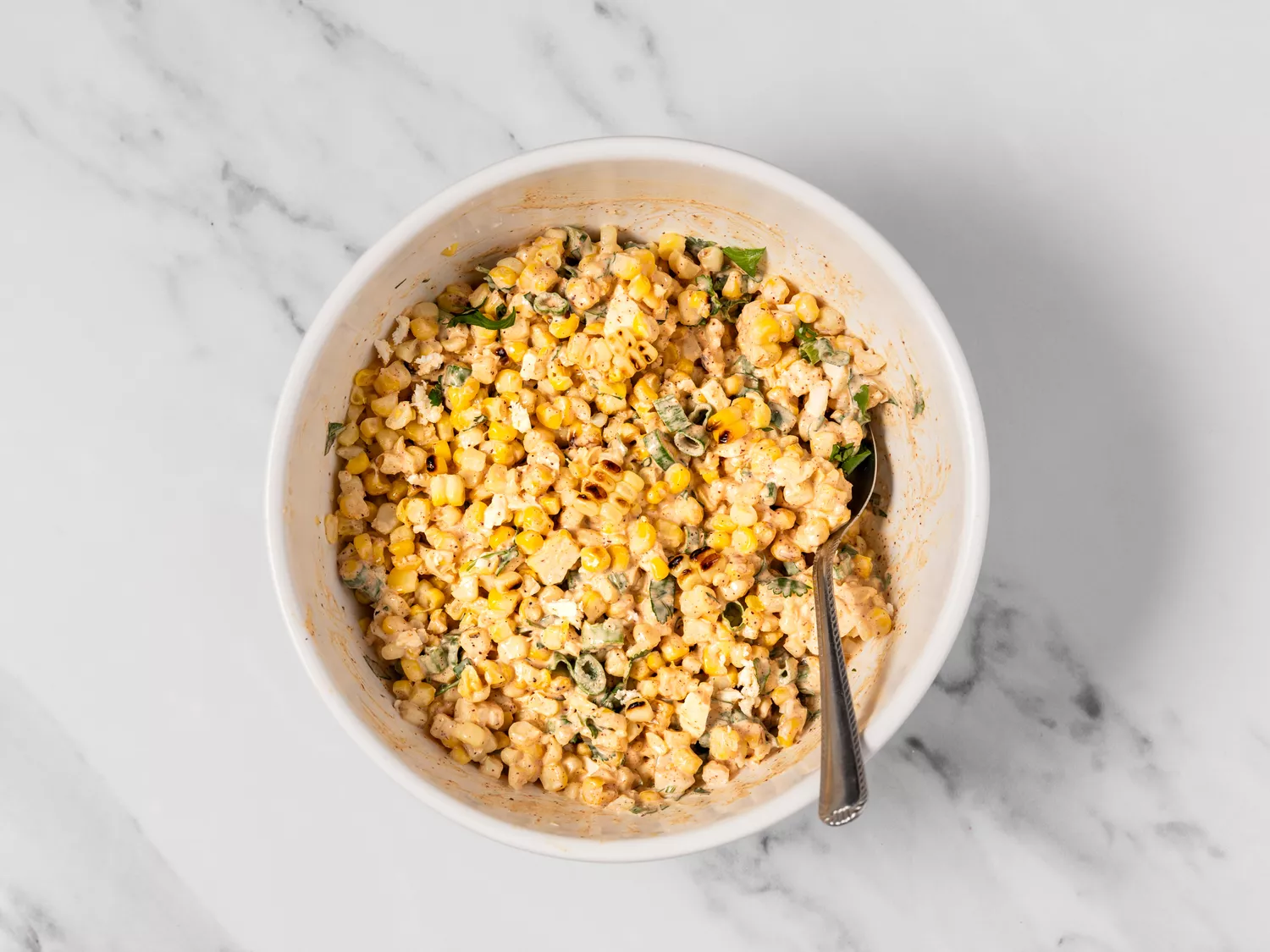 Bowl of elote salad with cheese, herbs, and dressing.