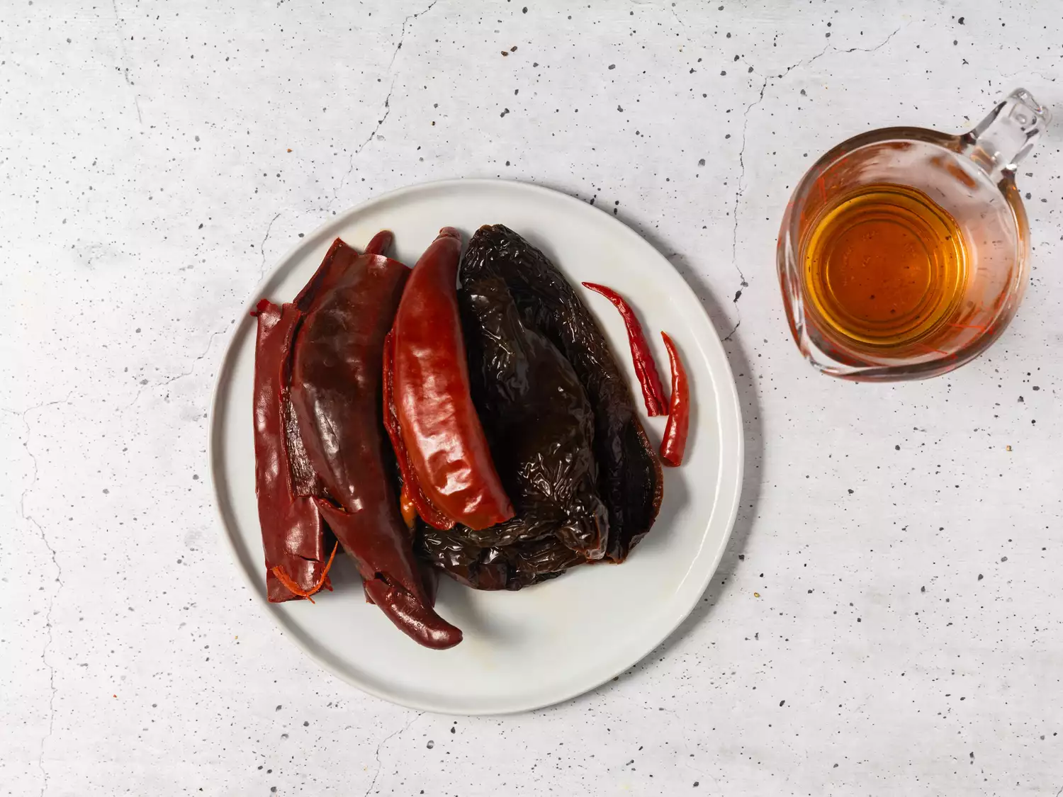 A bowl of rehydrated dried chili peppers, with a glass measuring cup of reserved cooking liquid