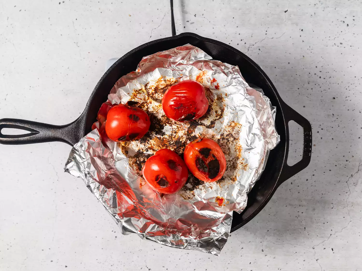 A cast iron pan lined with aluminum foil, with blackened tomatoes on top