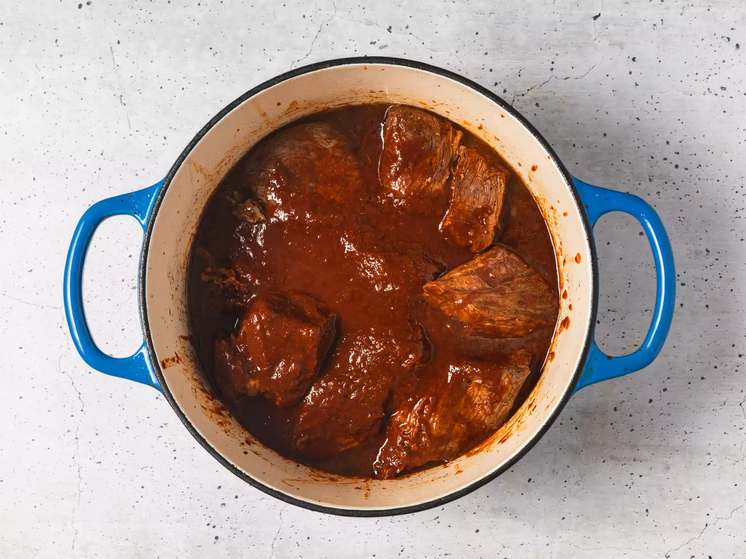 A dutch oven with seared pieces of beef covered in chili sauce
