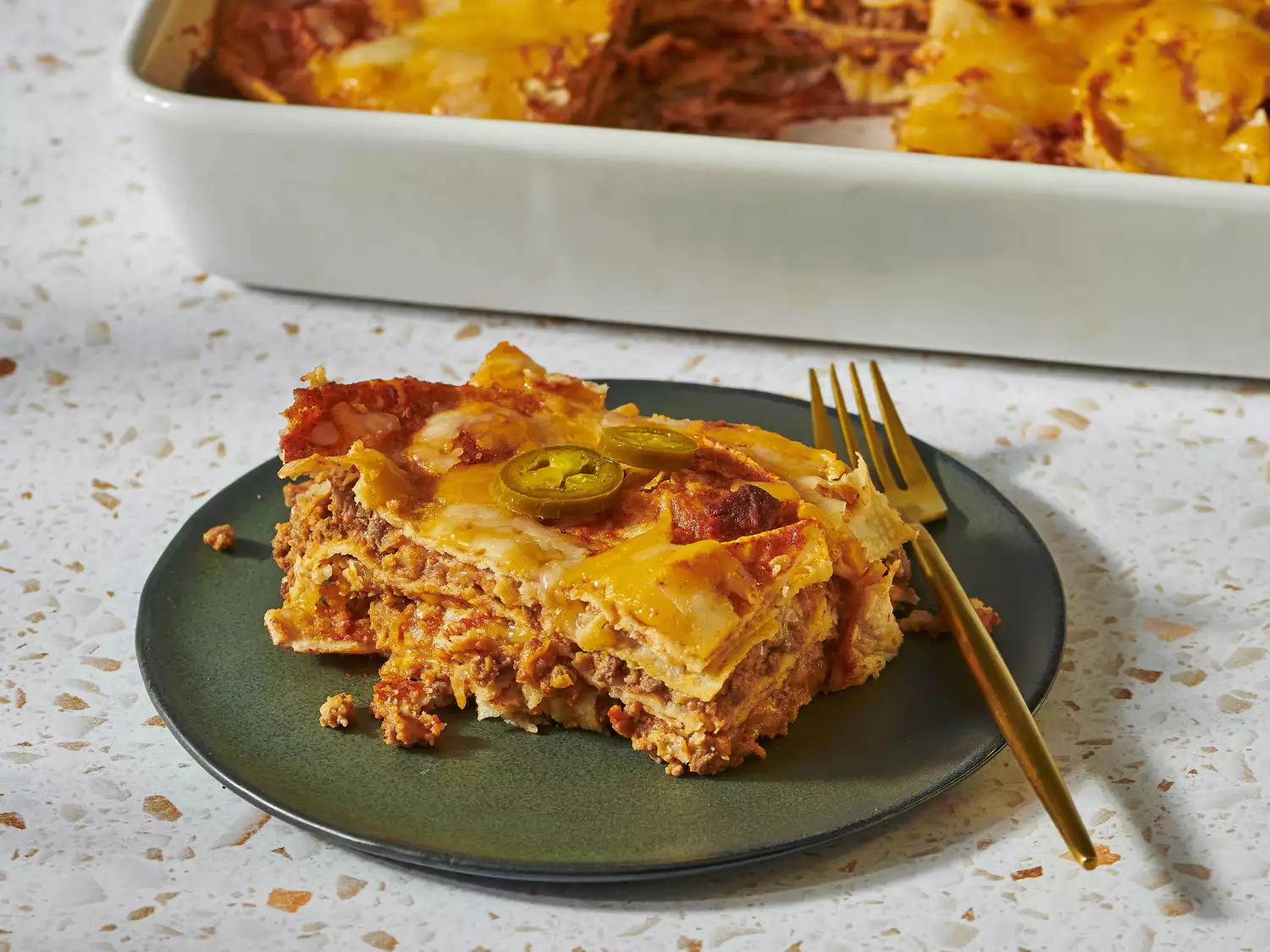 Slice of enchilada casserole on a green plate with fork.