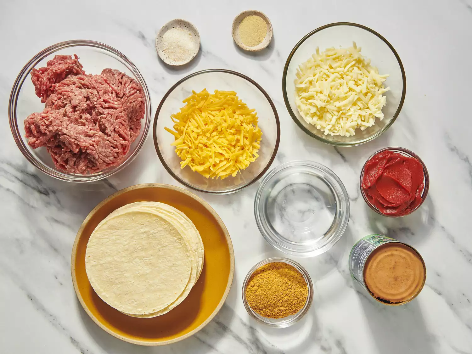 Ingredients for making enchiladas, including cheese, tortillas, and meat.