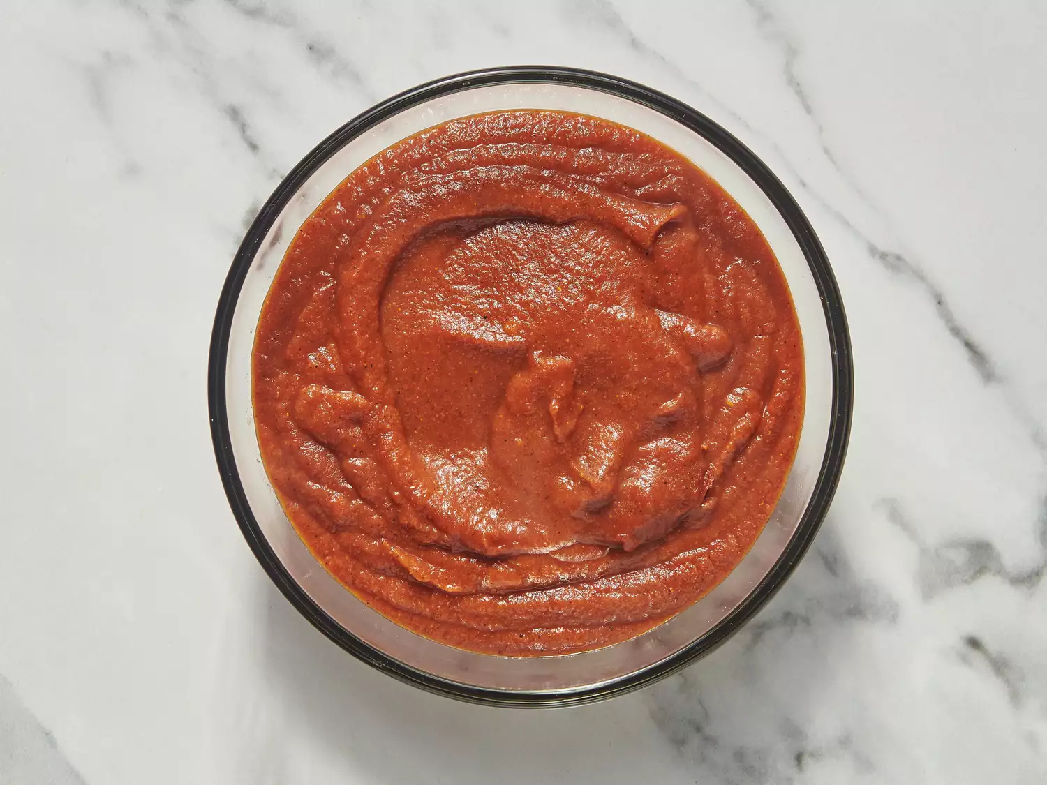 Bowl of smooth red enchilada sauce on marble countertop.