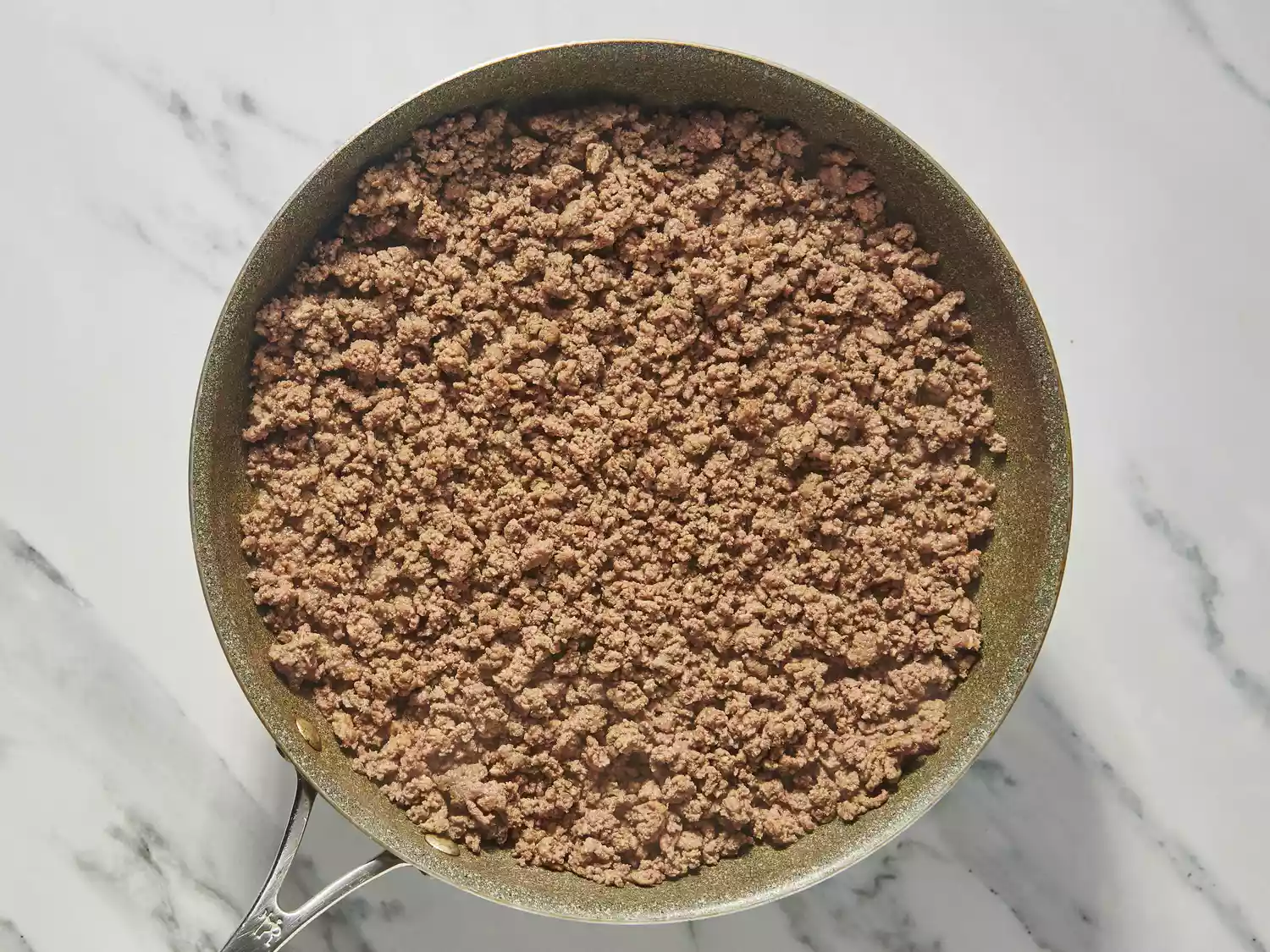 Cooked ground beef in a skillet on marble surface.