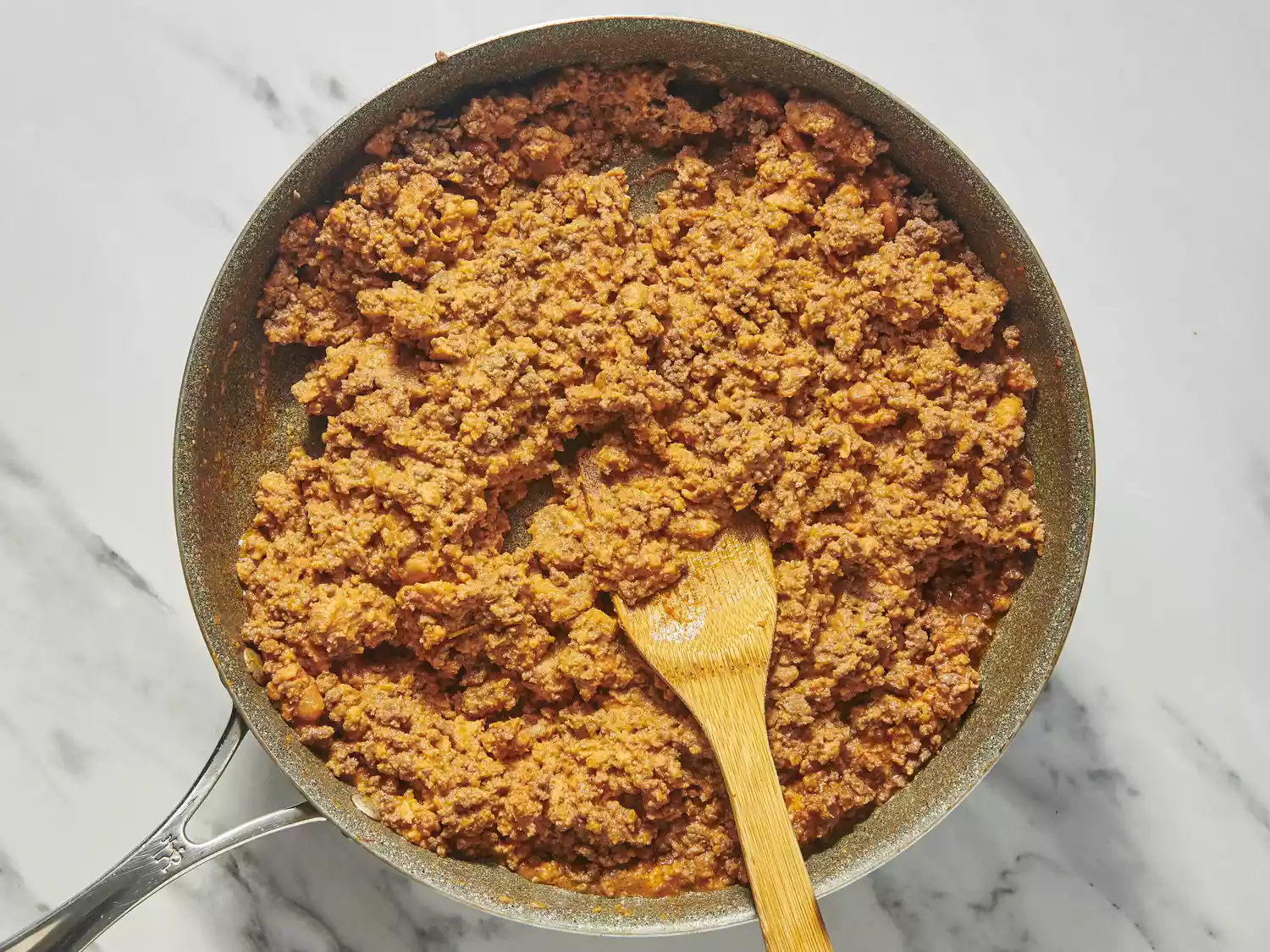 Skillet with seasoned ground beef and wooden spoon.