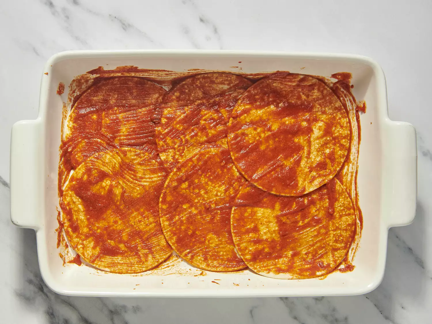 Tortillas coated with enchilada sauce in a baking dish.