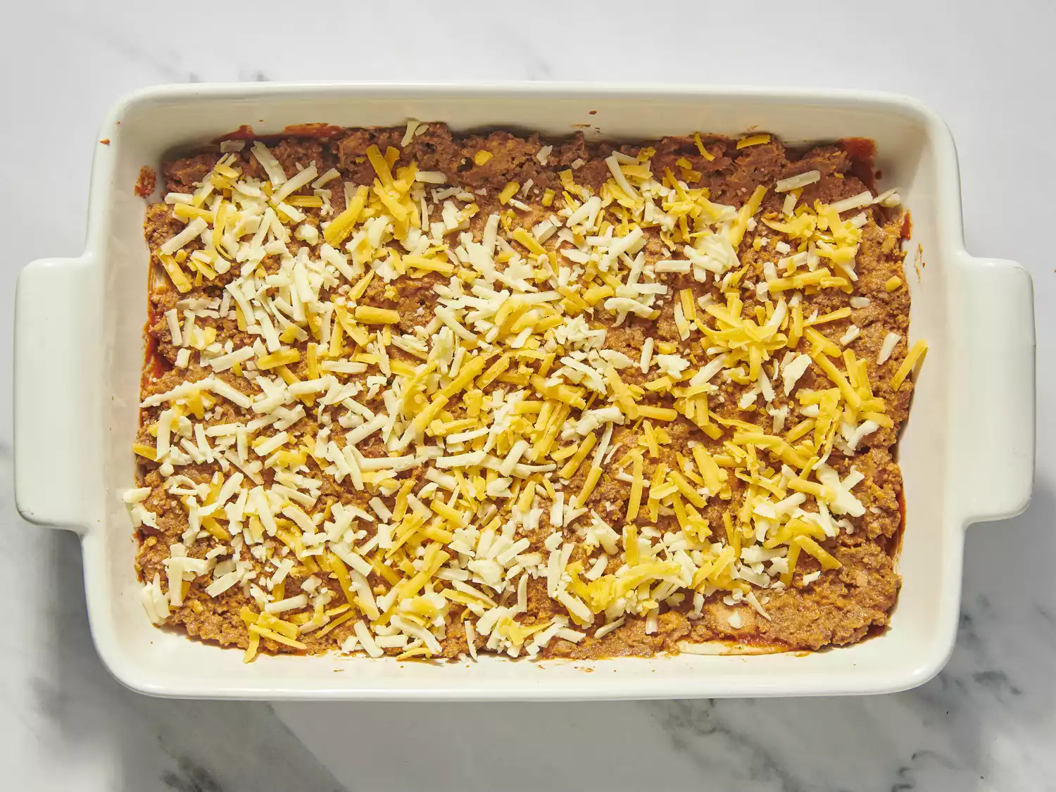 Baking dish layered with seasoned beef, cheese, and sauce.