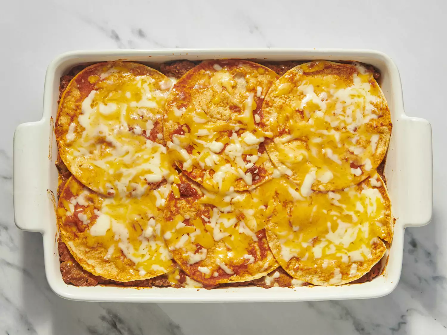 Baked enchiladas with melted cheese in a white baking dish.