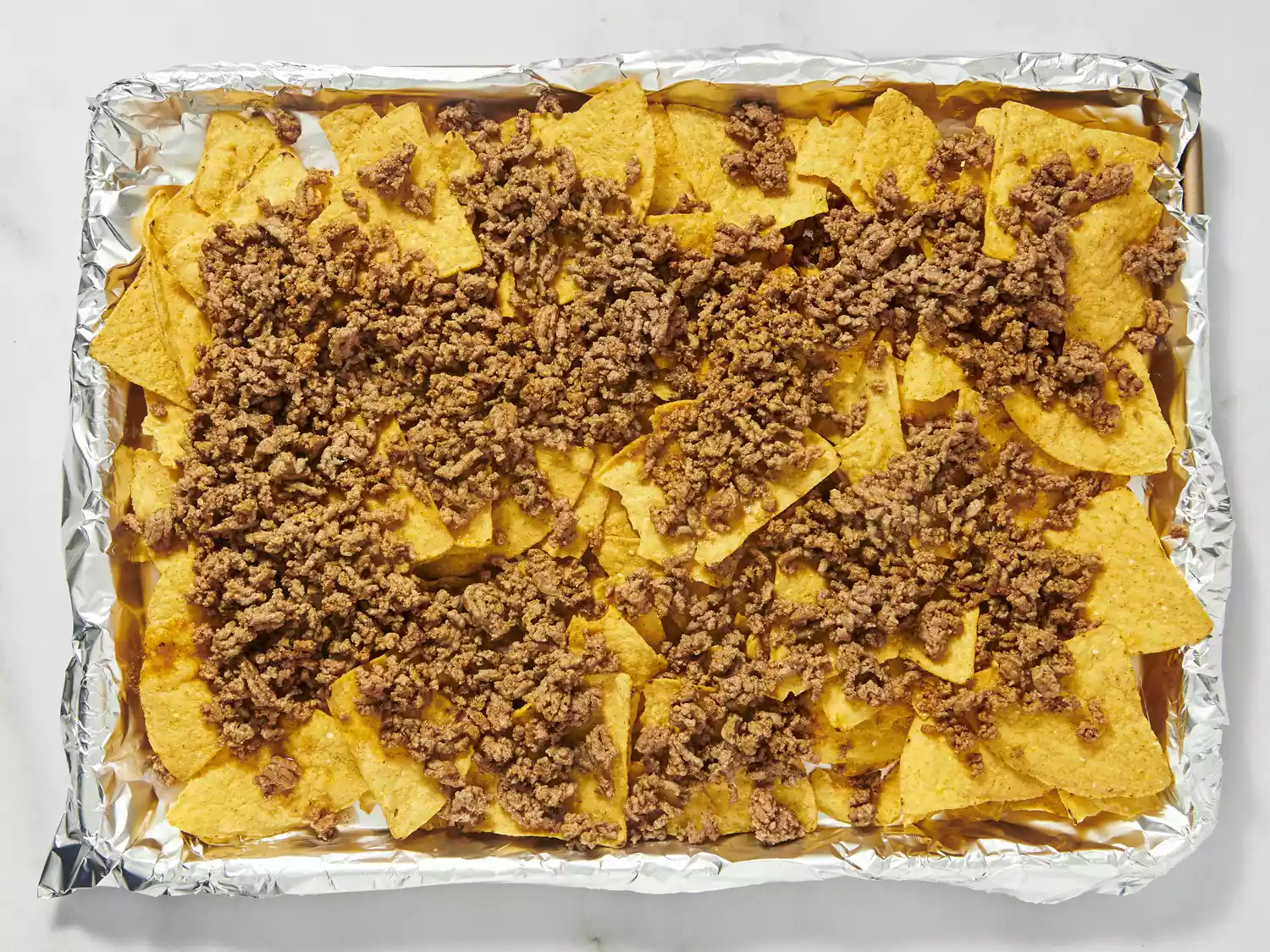 Tray of tortilla chips topped with seasoned ground beef.