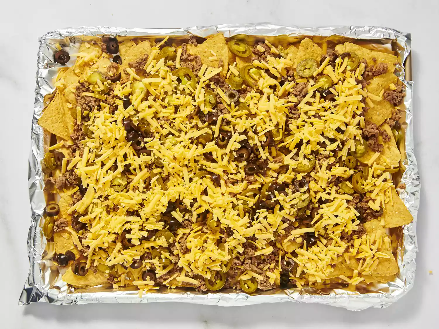 Nachos with shredded cheese, olives, and jalapeños before baking.