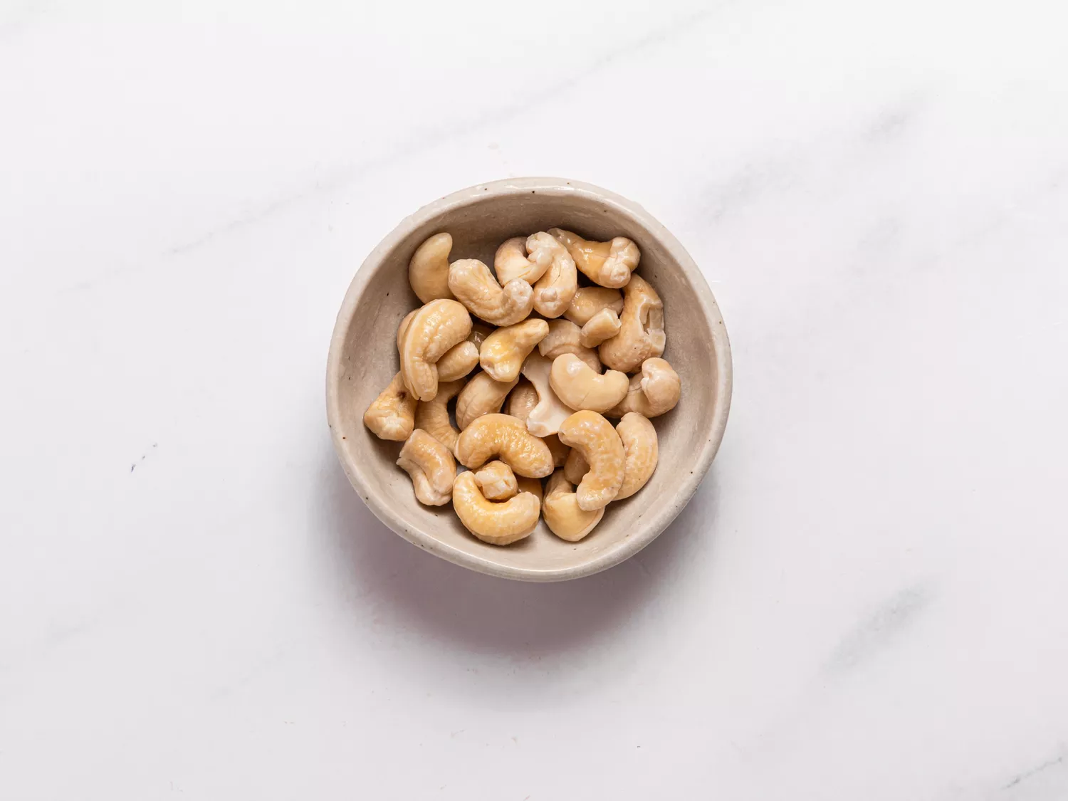 Bowl of raw cashews on a white background.