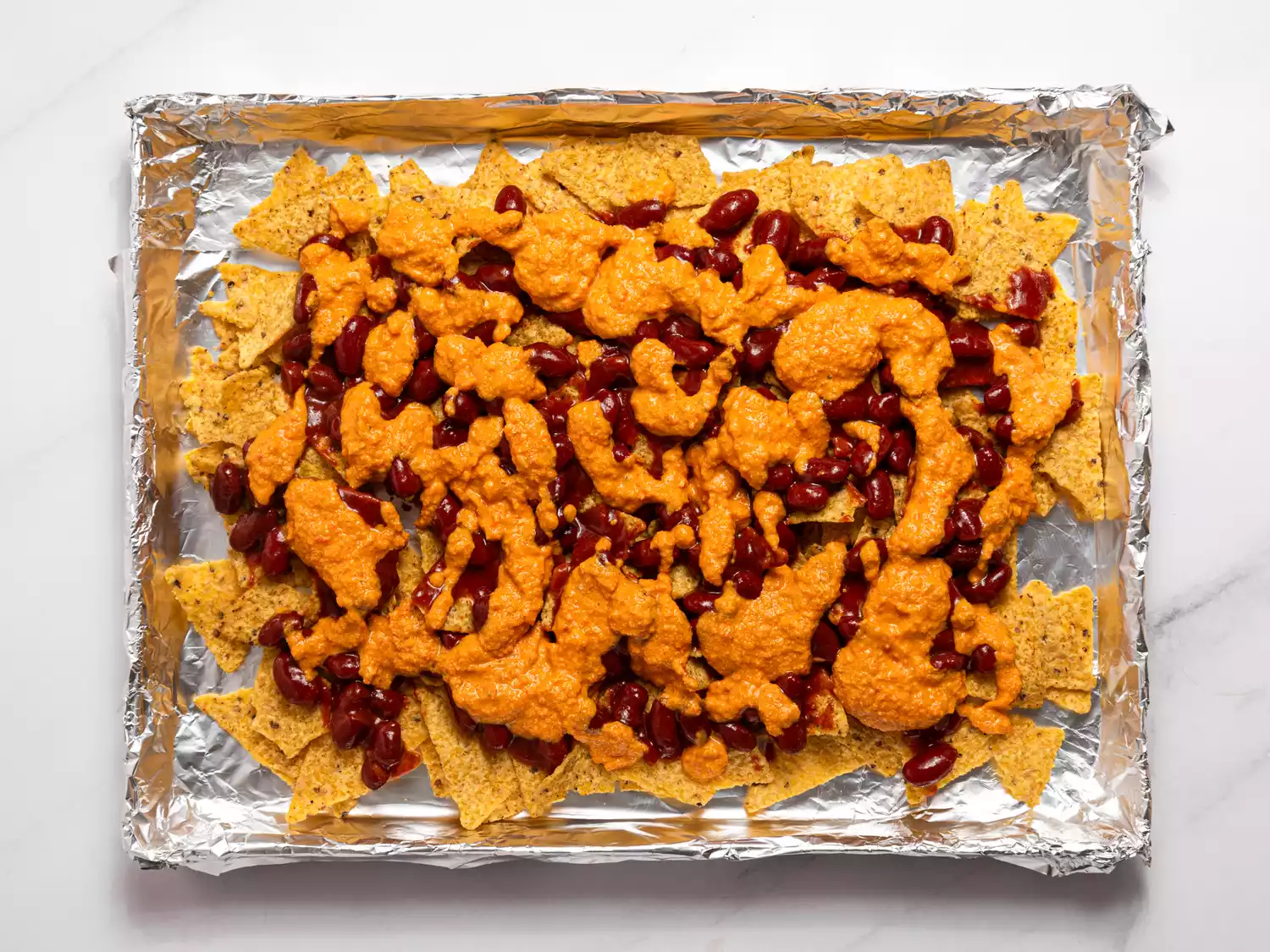 Unbaked nachos with beans and cheese sauce.