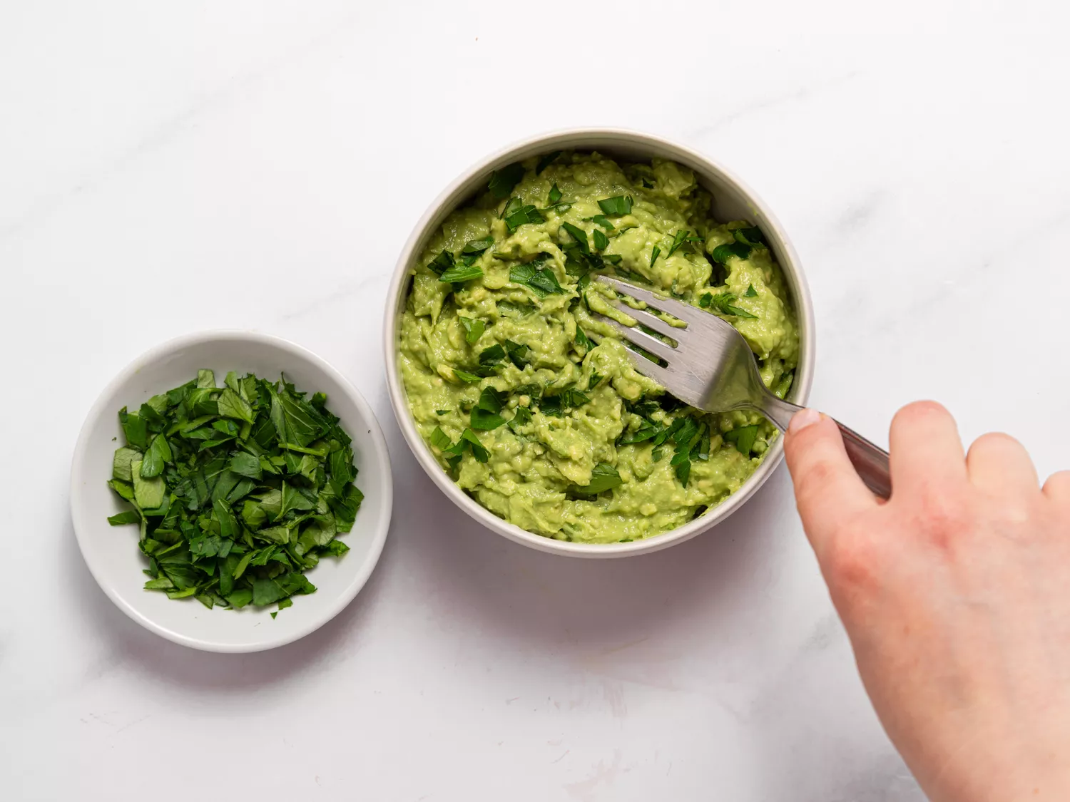 Guacamole being mixed with fresh herbs in a bowl.