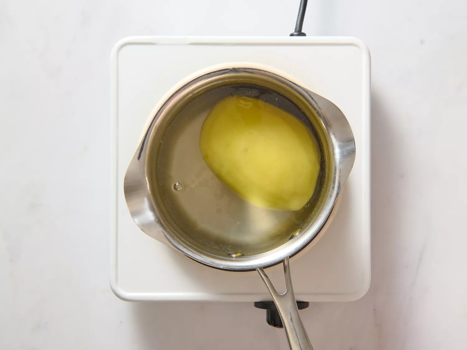 A pot of water with a whole, peeled potato