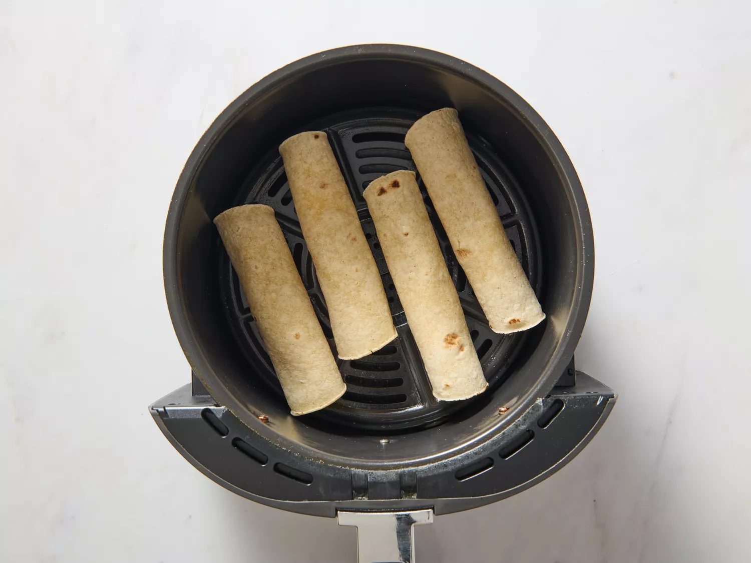 An air fryer basked with four potato taquitos