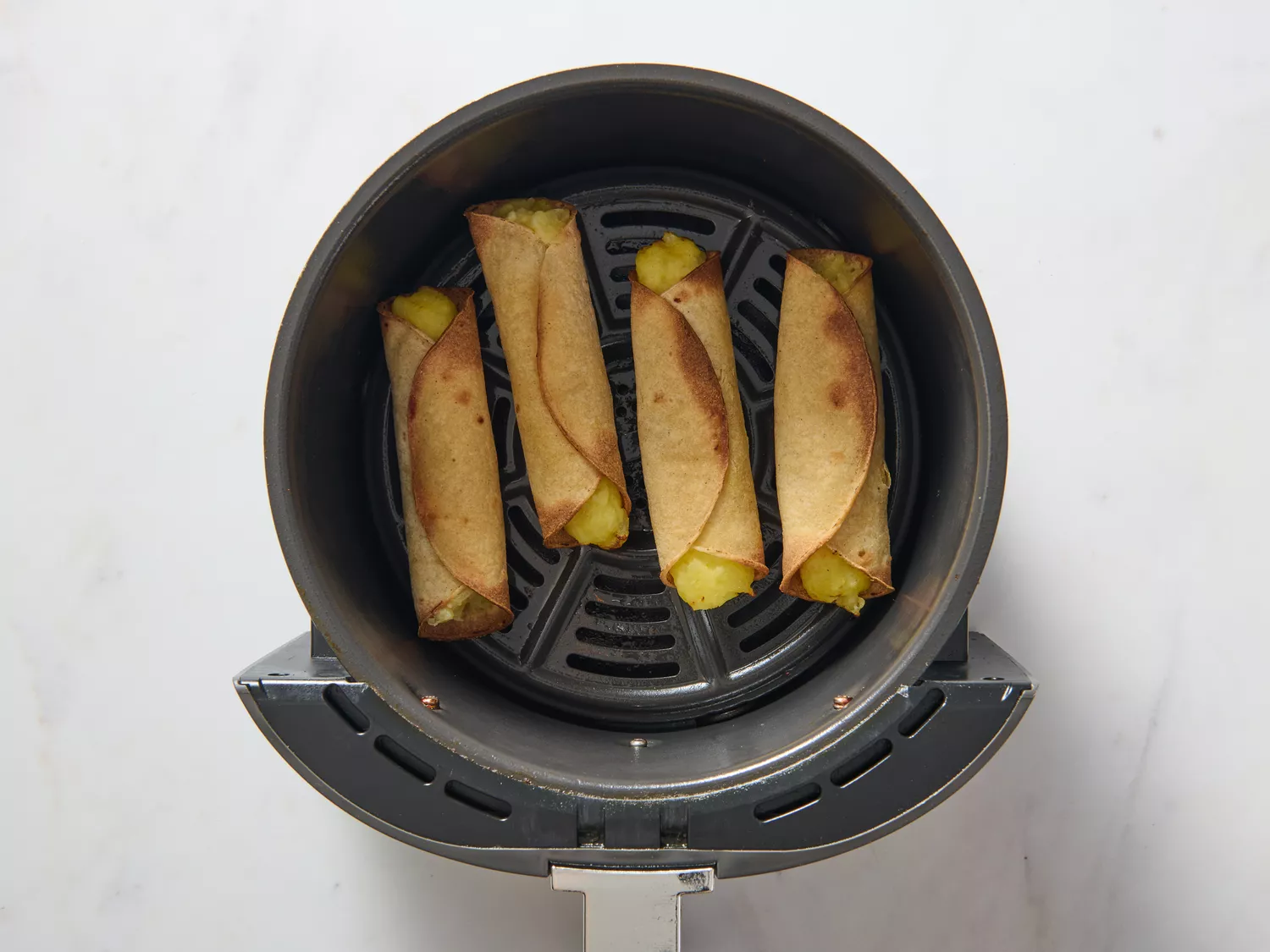 An air fryer basket with four cooked vegan potato taquitos