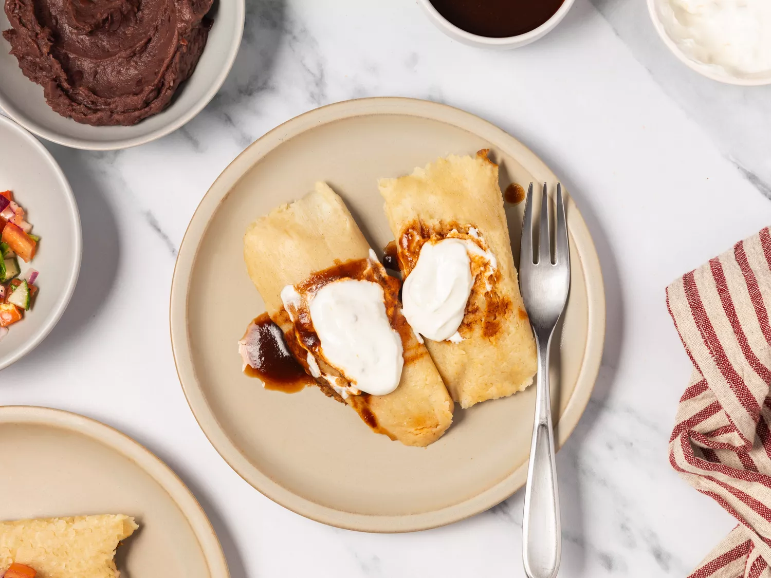 Tamales on a plate topped with chile sauce and sour cream.
