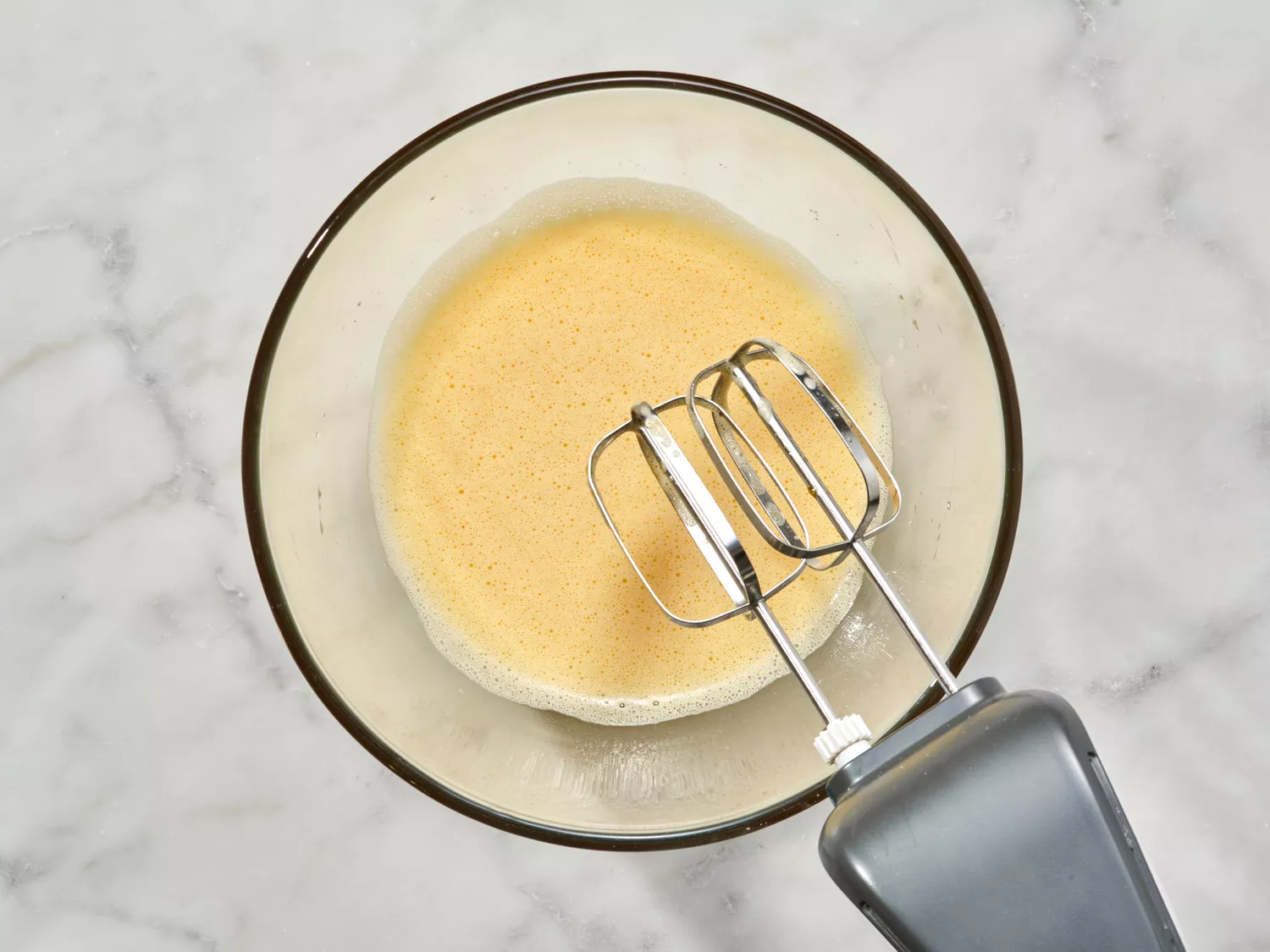 Beaten egg mixture in a glass bowl with beaters.