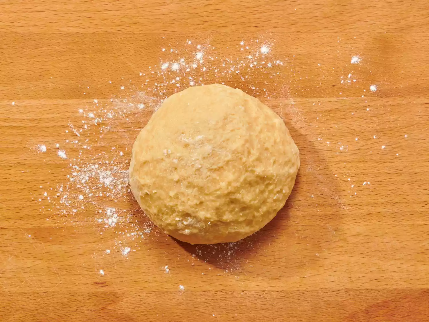 Ball of dough dusted with flour on a wooden surface.