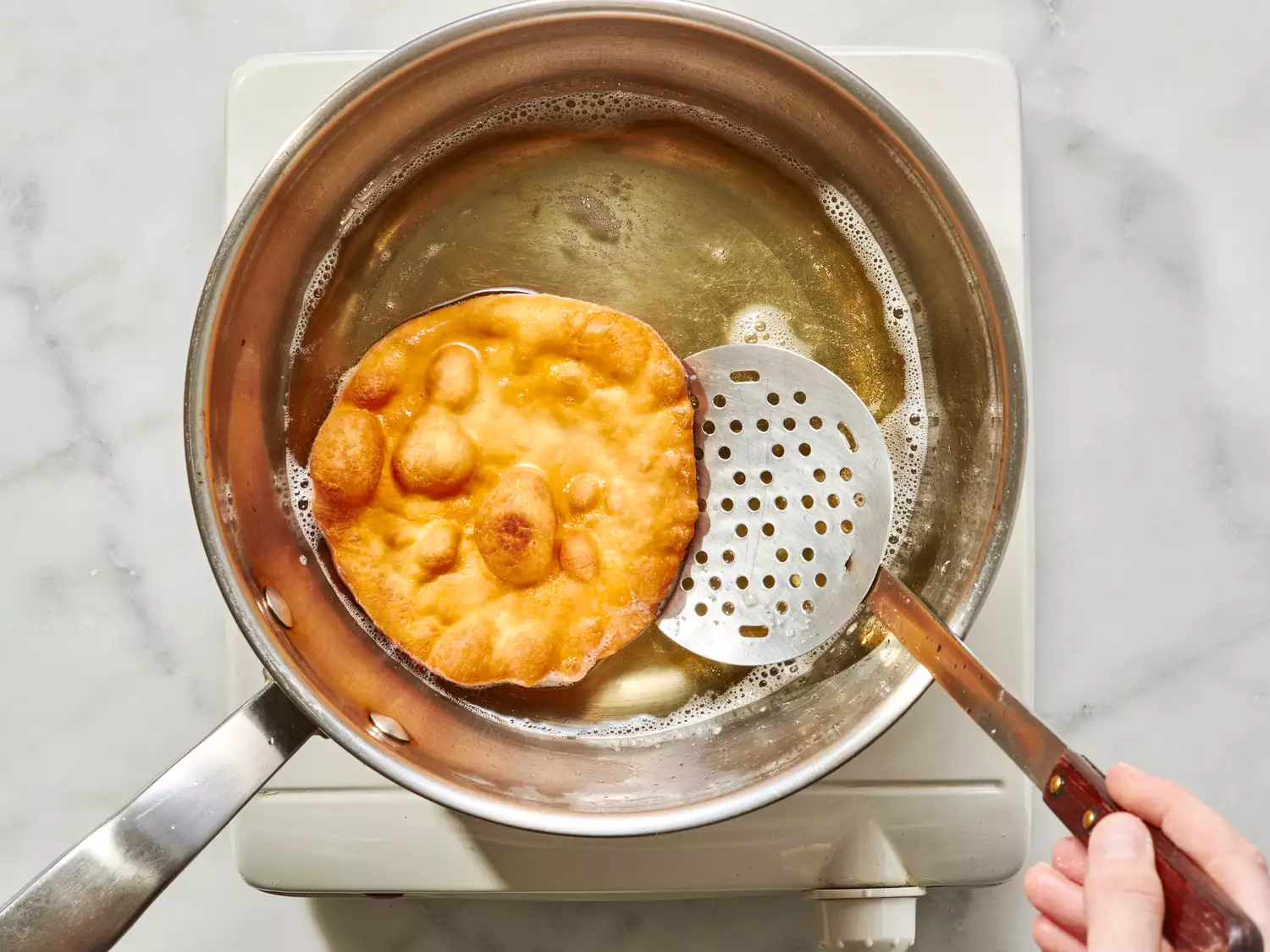 Buñuelo frying in oil, scooped out with a slotted spoon.