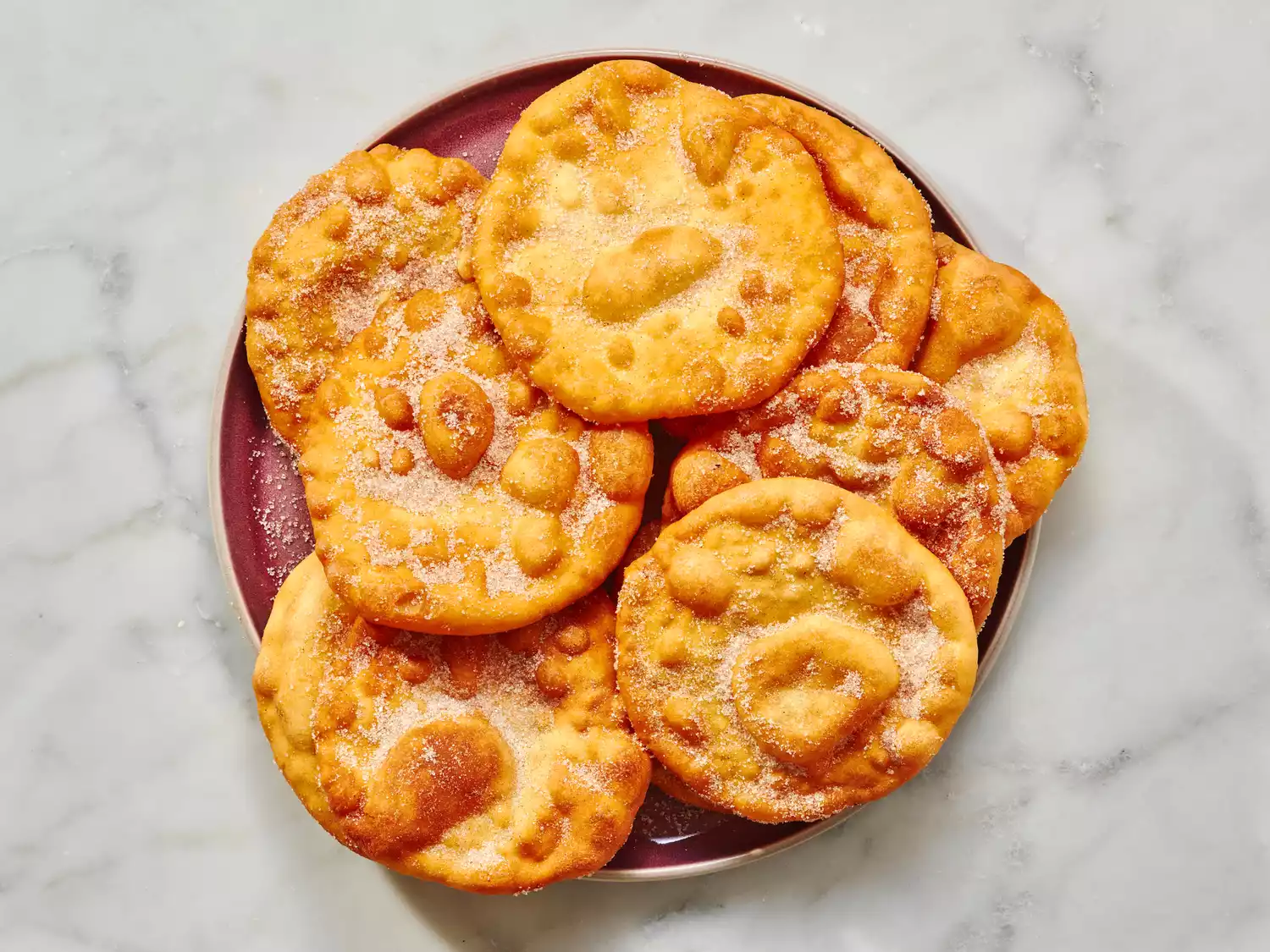Plate of freshly fried buñuelos coated in sugar.