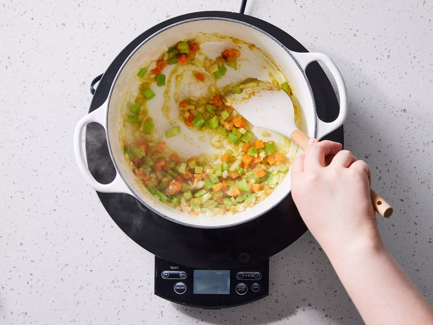 A large pot with onion, celery, carrots, butter, flour, and curry powder being stirred with a rubber spatula