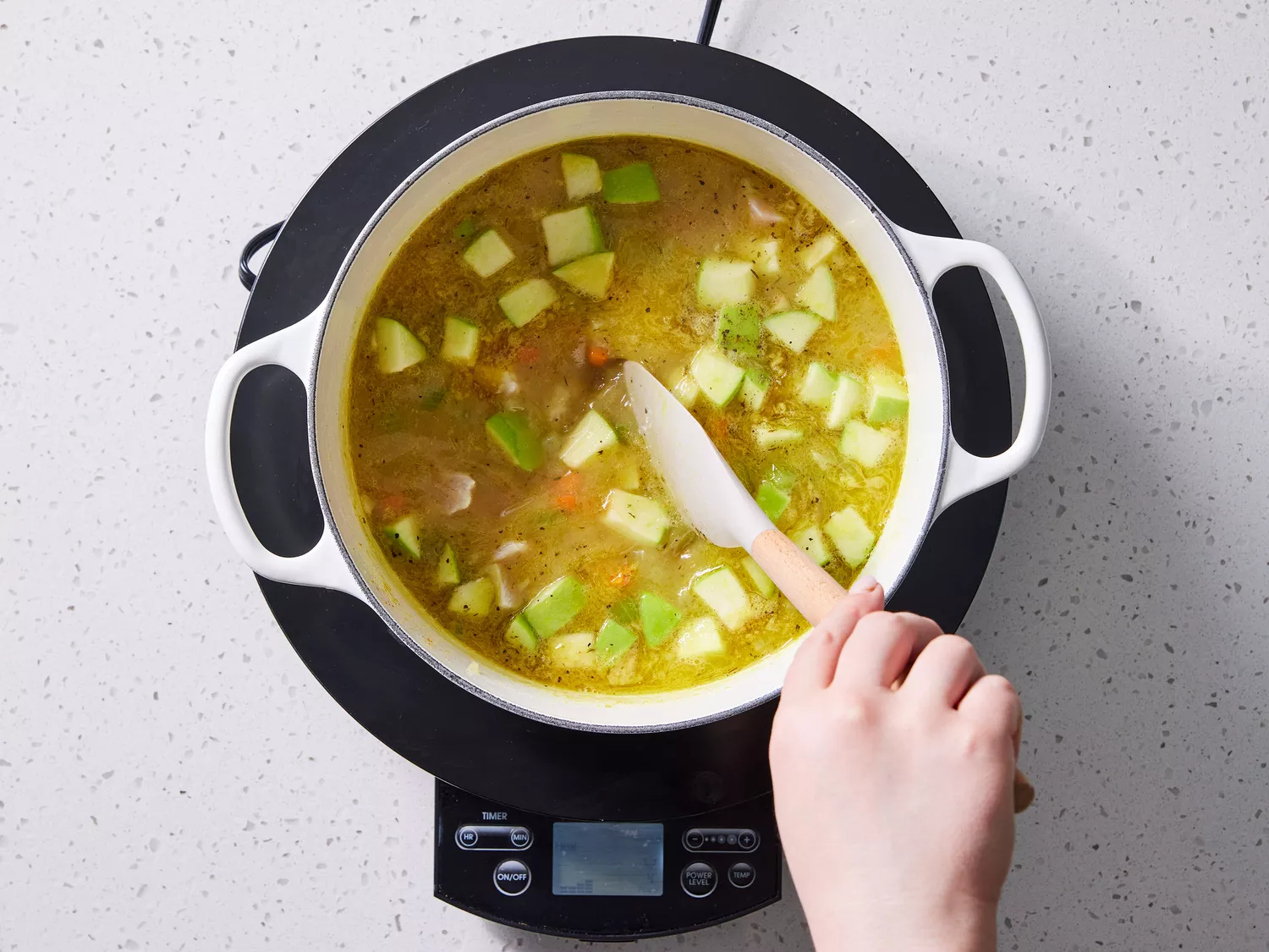 A large pot of soup with chopped apples being stirred with a rubber spatula