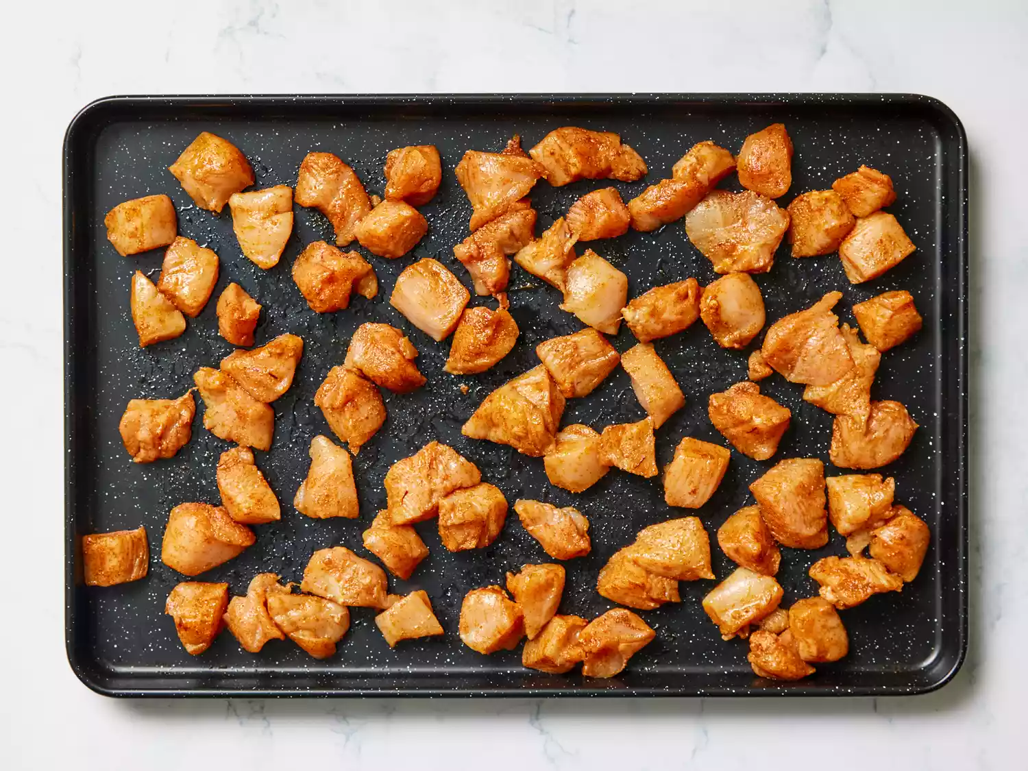 A baking sheet with pieces of chicken breast coated in oil and tandoori masala