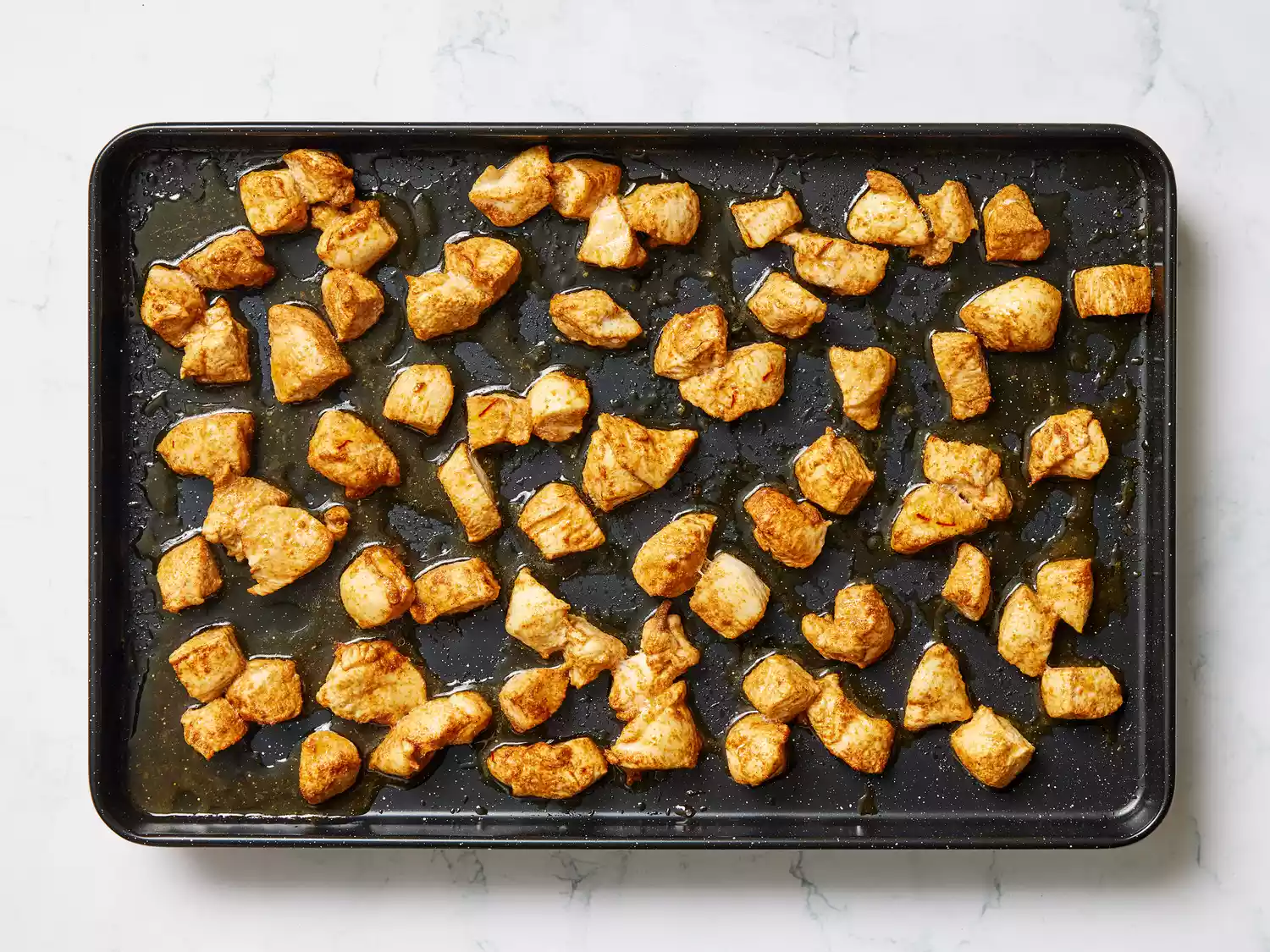 A baking sheet with baked pieces of seasoned chicken