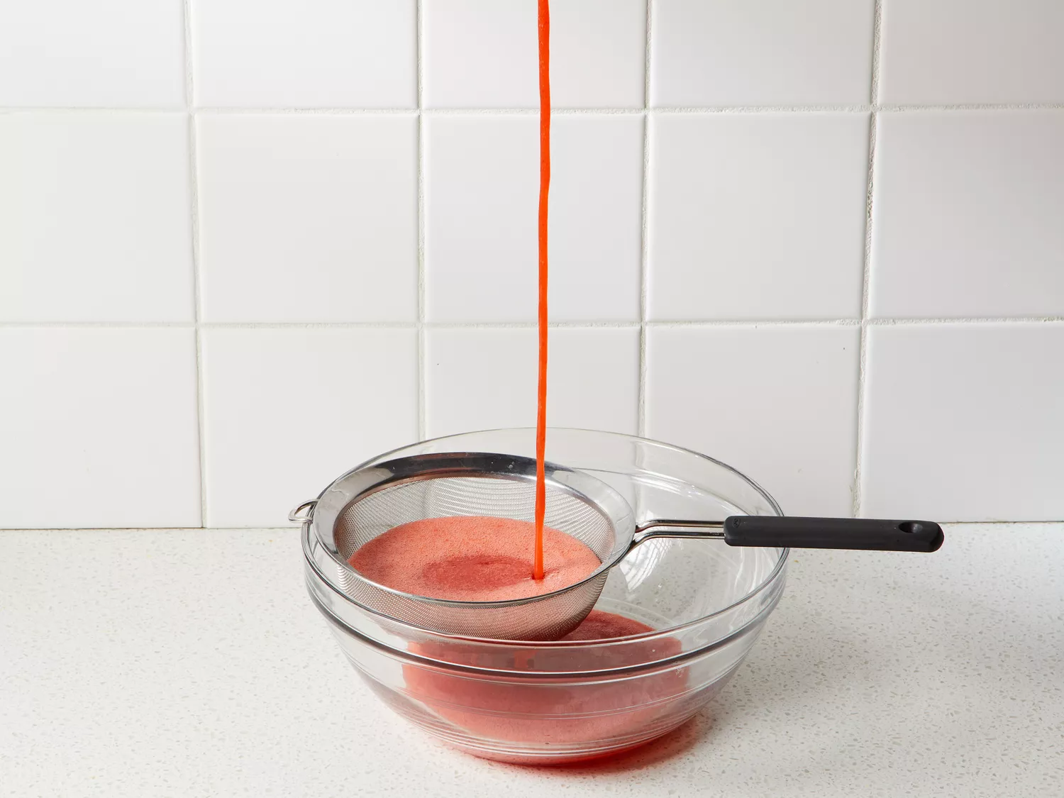 A strainer with strawberry pulp and seeds set over a large bowl of strawberry juice