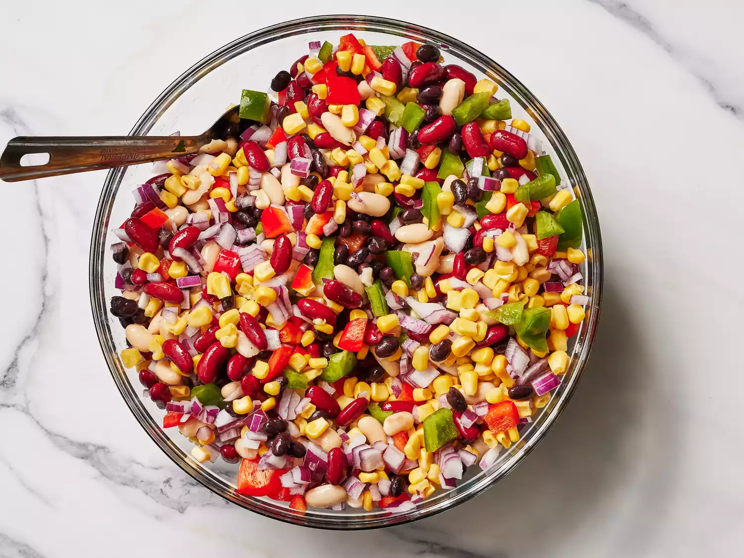 A large bowl with beans, chopped bell peppers, corn, and chopped onion