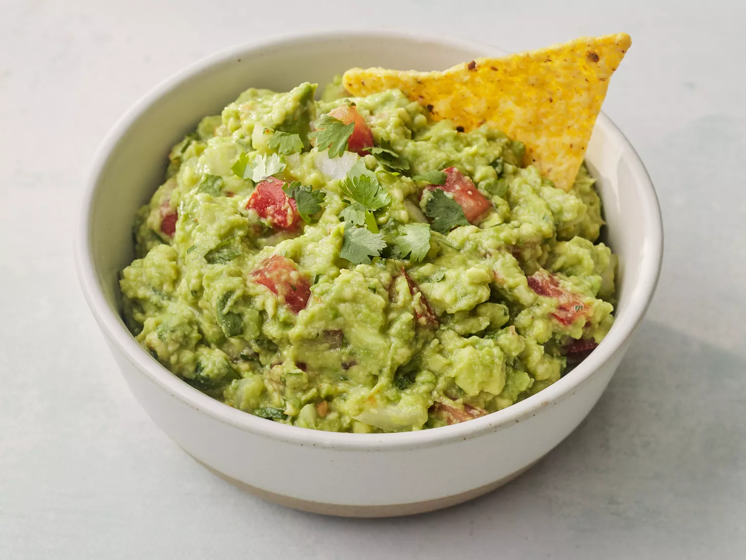 A bowl of guacamole topped with fresh cilantro, with a tortilla chip sticking out of the top