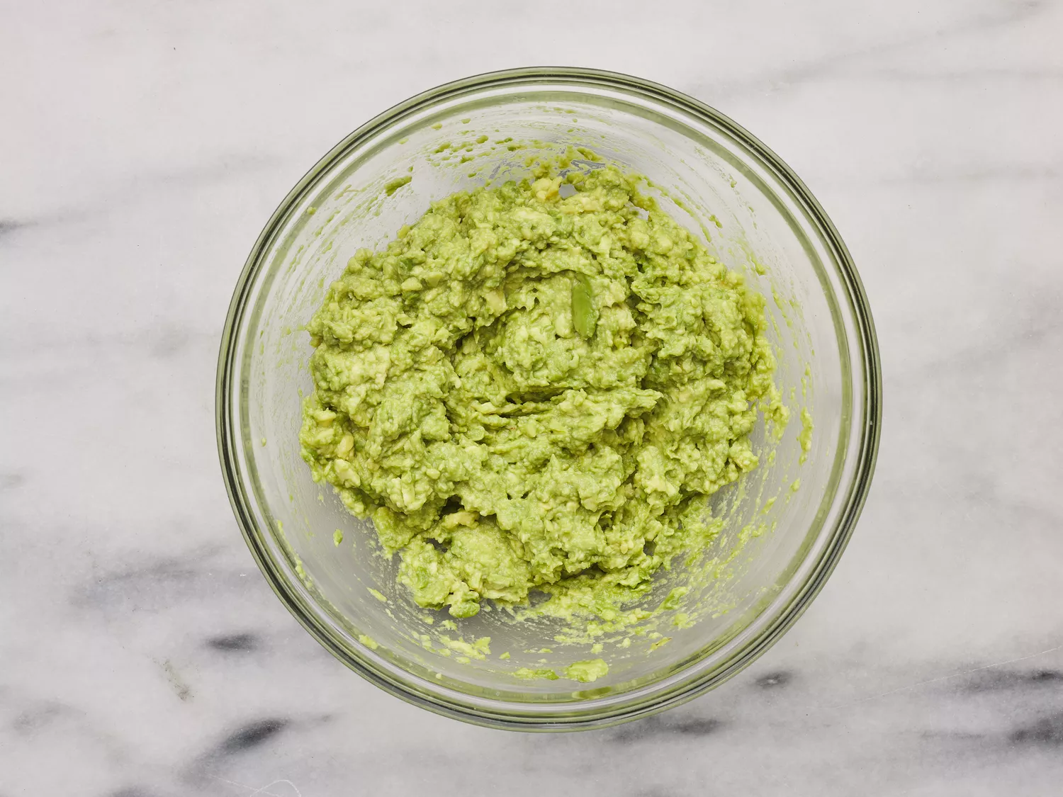 A bowl of mashed avocado with lime juice, salt, tomatoes, onion, cilantro, and garlic