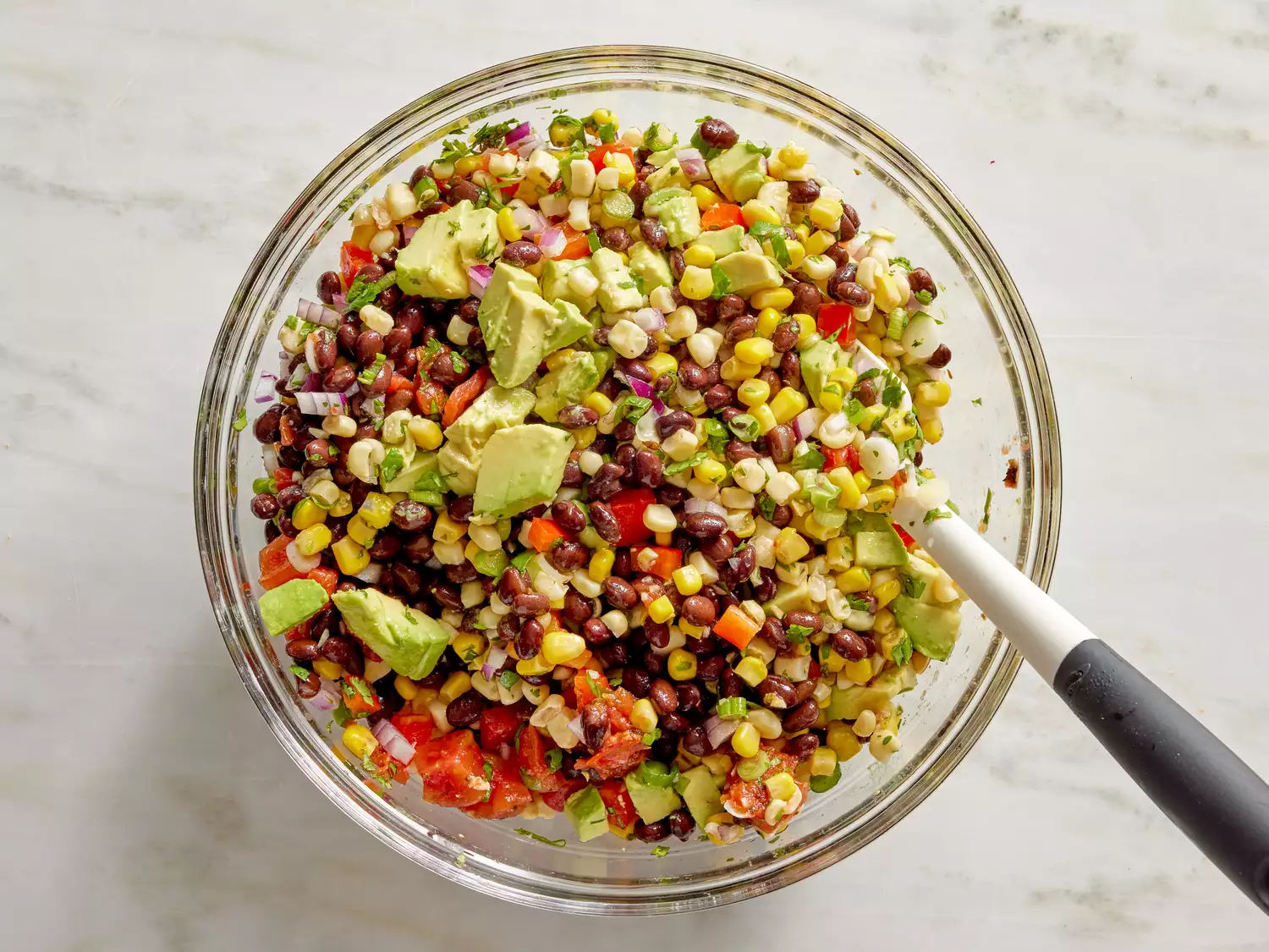A bowl of cilantro, black bean, and corn salsa with chunks of avocado, dressed with lime juice