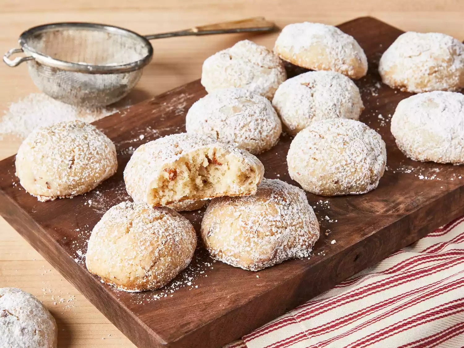 Mexican wedding cookies served on a wooden board, with a bite takes out of one