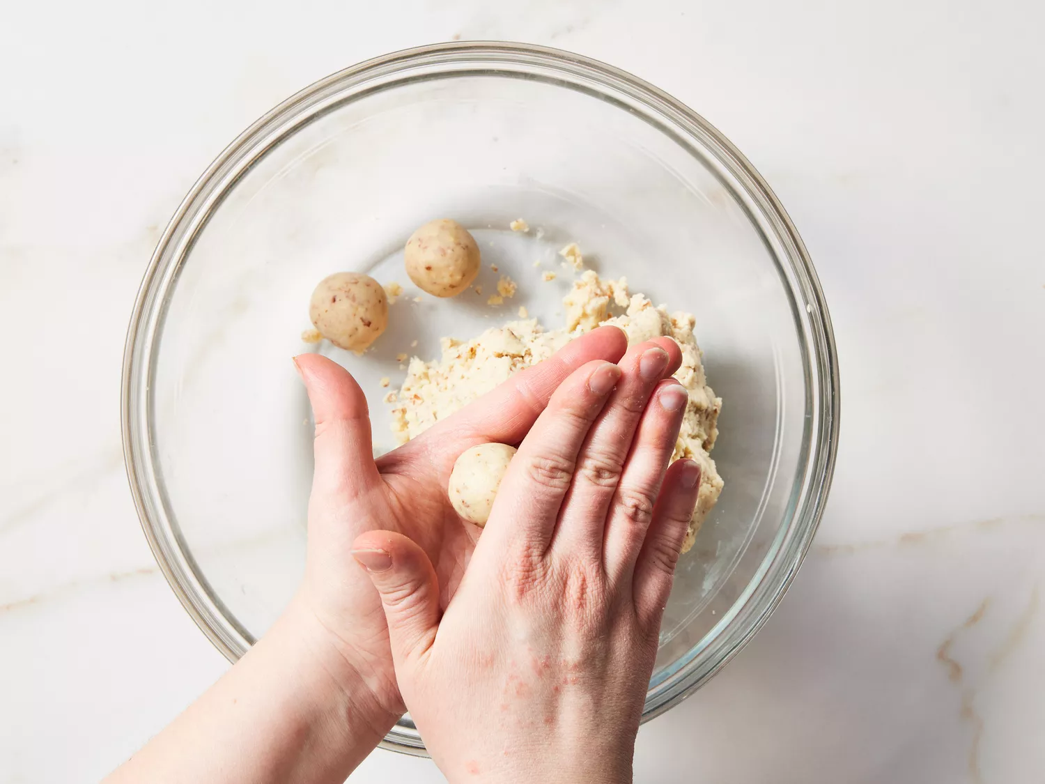 Two hands rolling cookie dough into small balls