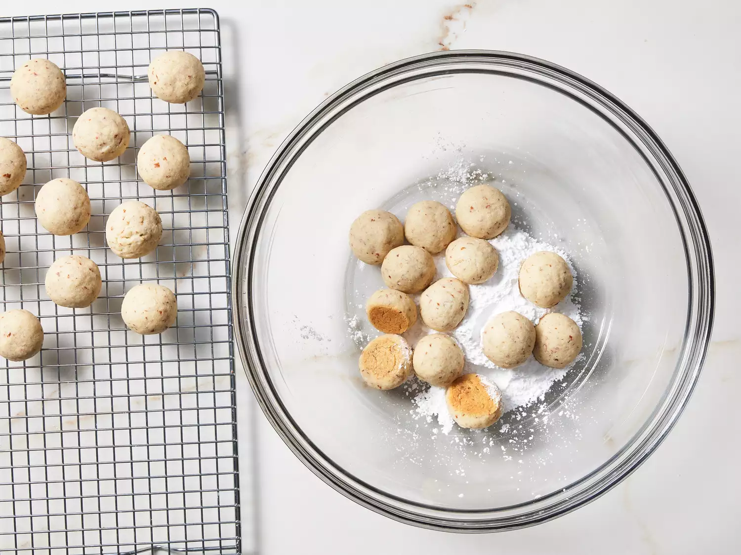 A large glass bowl with Mexican wedding cookies being tossed in powdered sugar