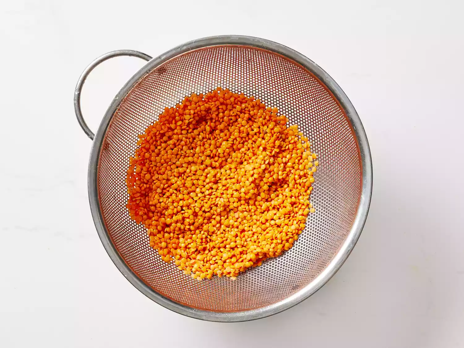 A colander with rinsed red lentils