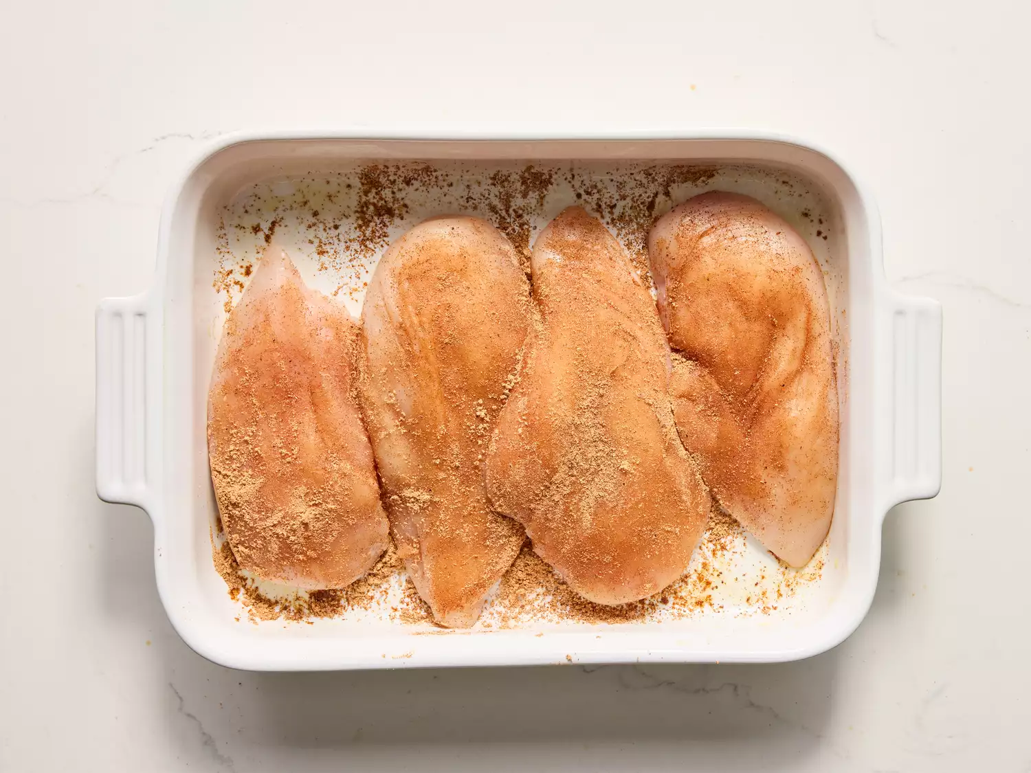 A baking dish with raw chicken breasts topped with seasoning mix