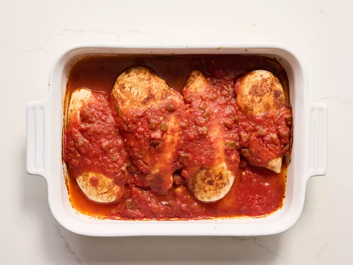 A baking dish with four cooked chicken breasts in salsa