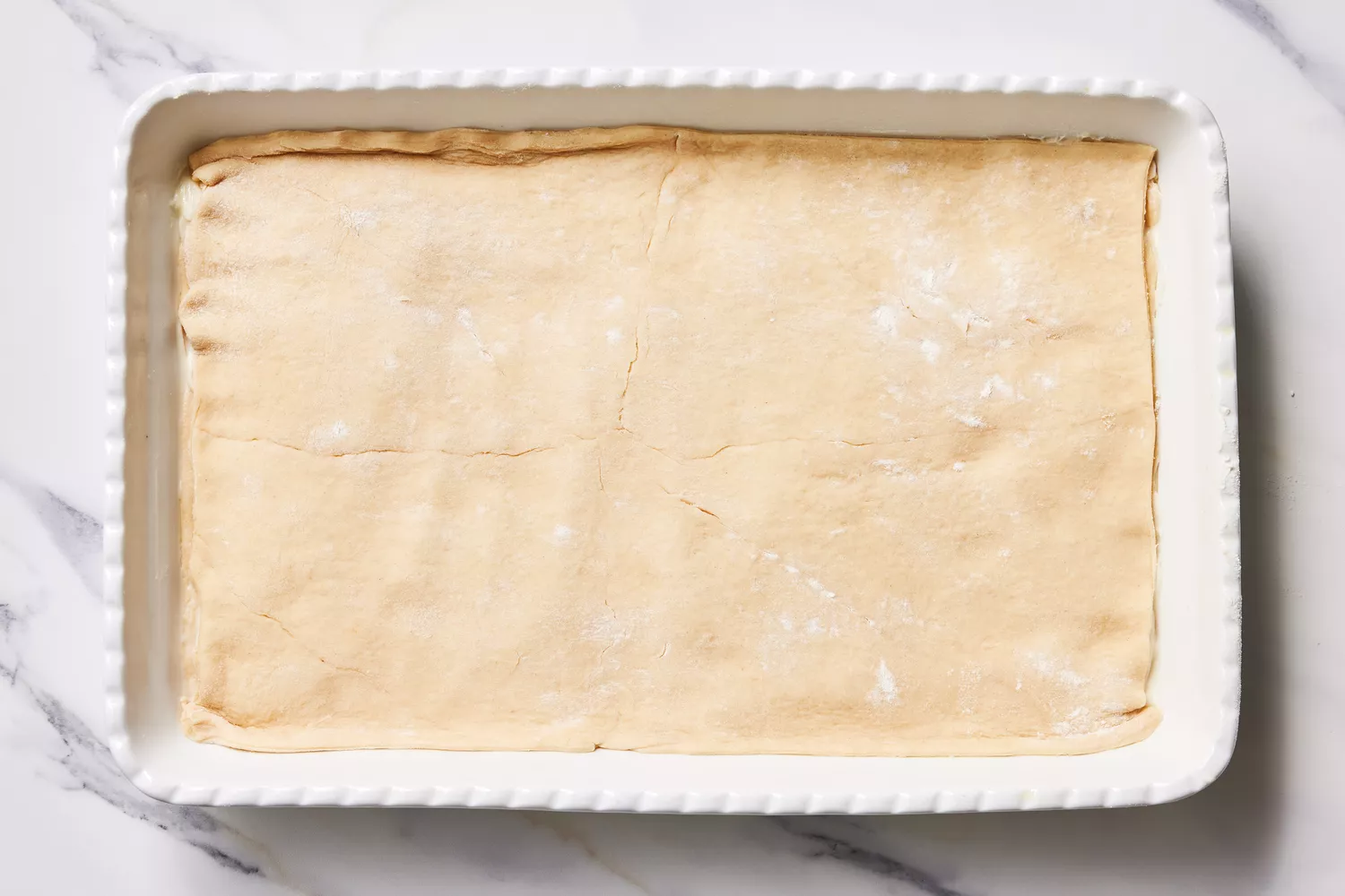 A baking dish with crescent dough topped with sweetened cream cheese mixture, topped with another sheet of crescent dough