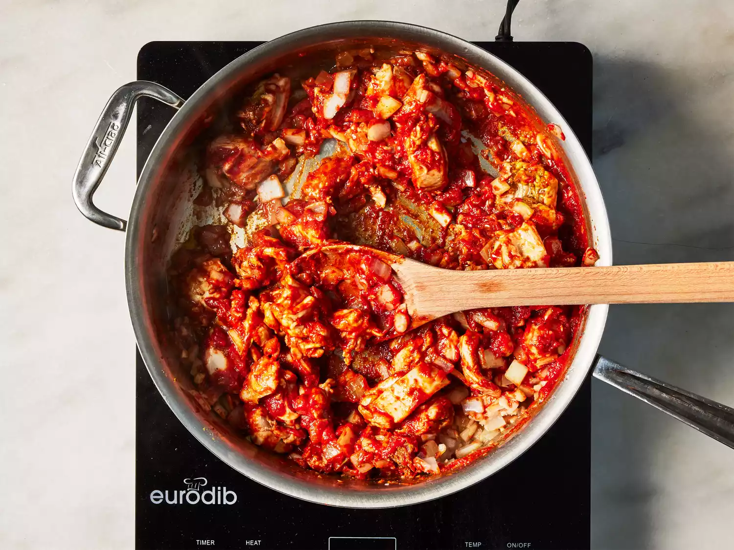 A pan with pieces of chicken, garlic, and onions cooking down in tomato paste and spices