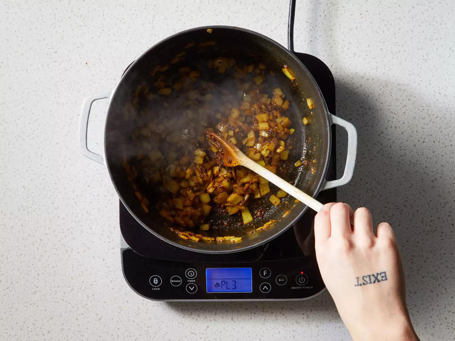 A wooden spoon stirring chopped onion, garlic, and oil into toasted spices in a pot