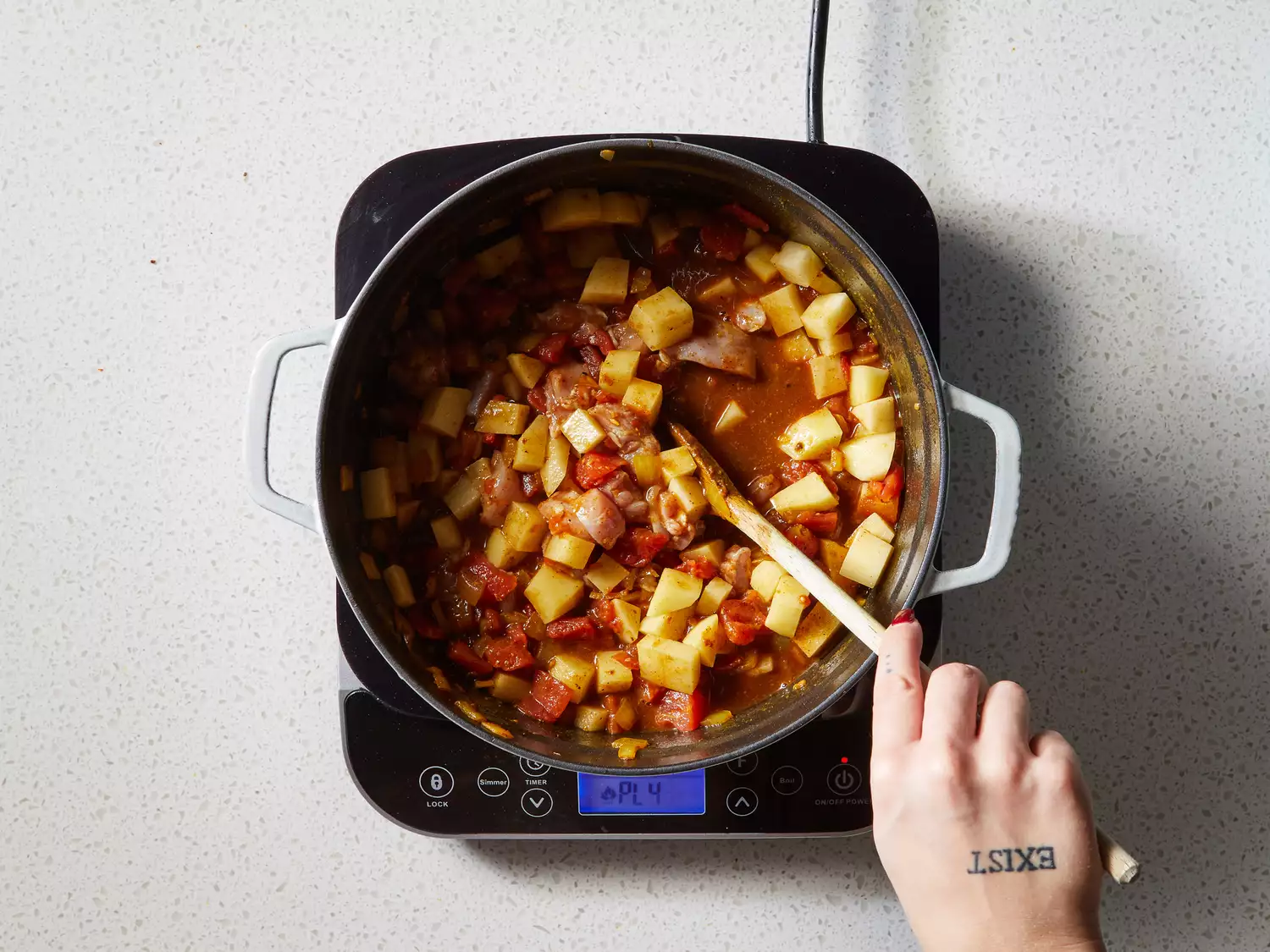 A pot with potatoes and chicken cooking down in spiced tomato sauce