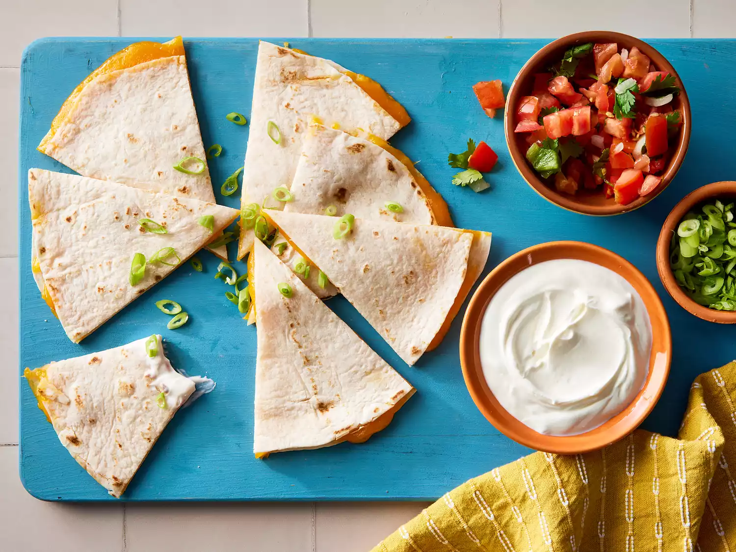 A sliced cheese quesadilla, served with pico de gallo, sour cream, and sliced green onions