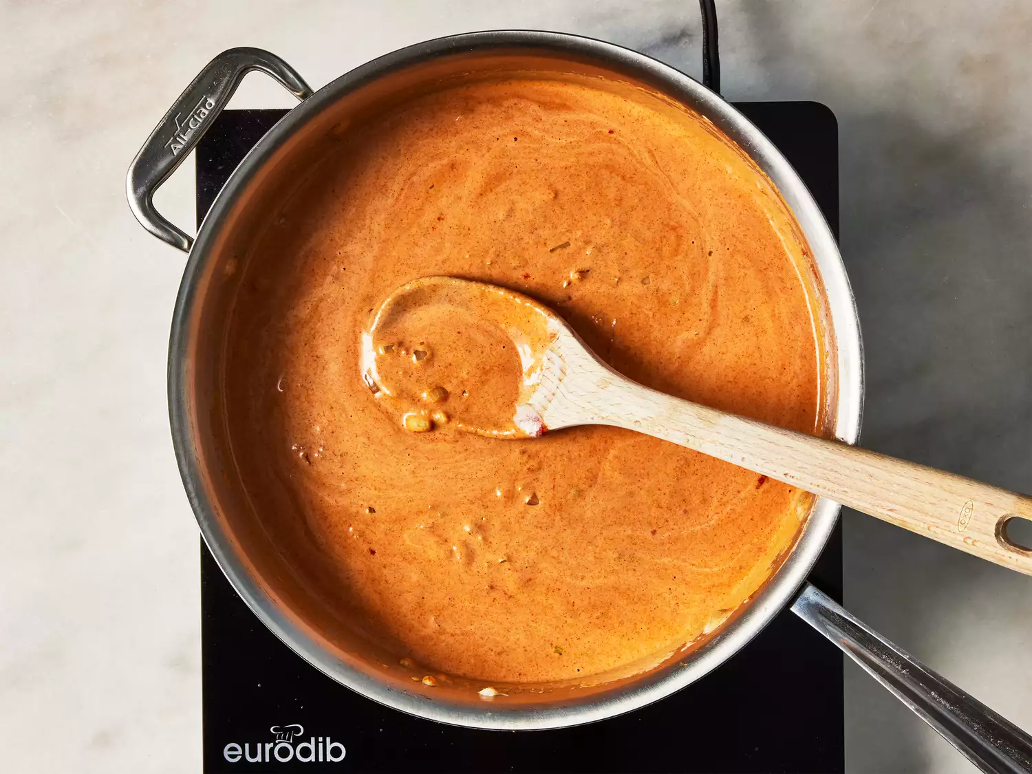 A large pan of creamy tomato sauce being stirred with a wooden spoon