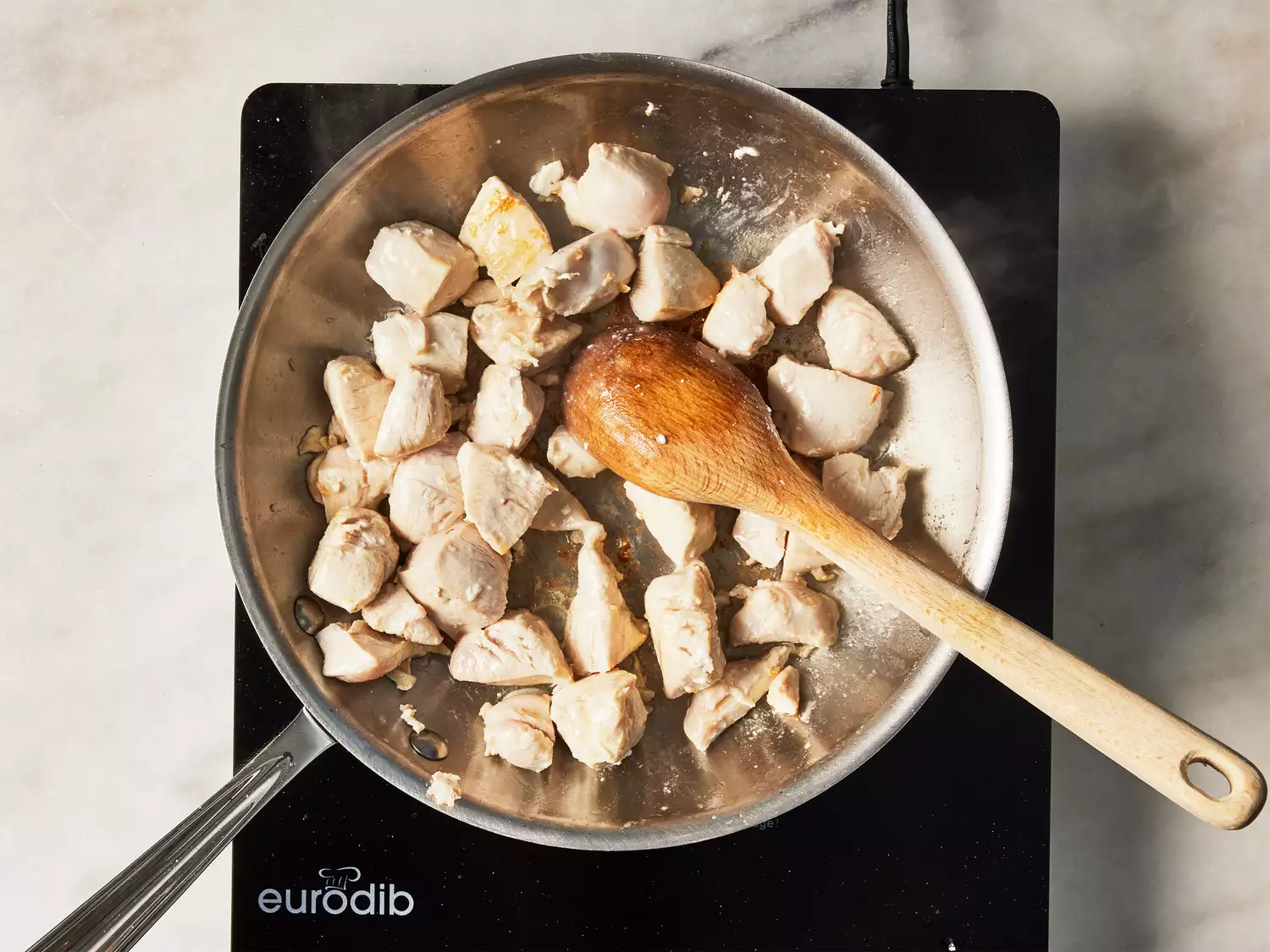 A pan of seared cubed chicken being stirred with a wooden spoon