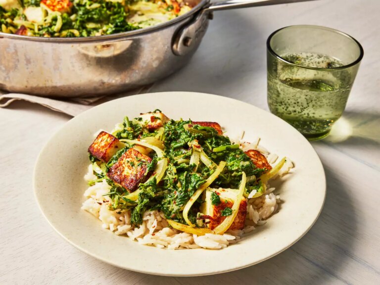 A bowl of saag paneer, served over rice, with a pan of saag paneer in the backgrounf
